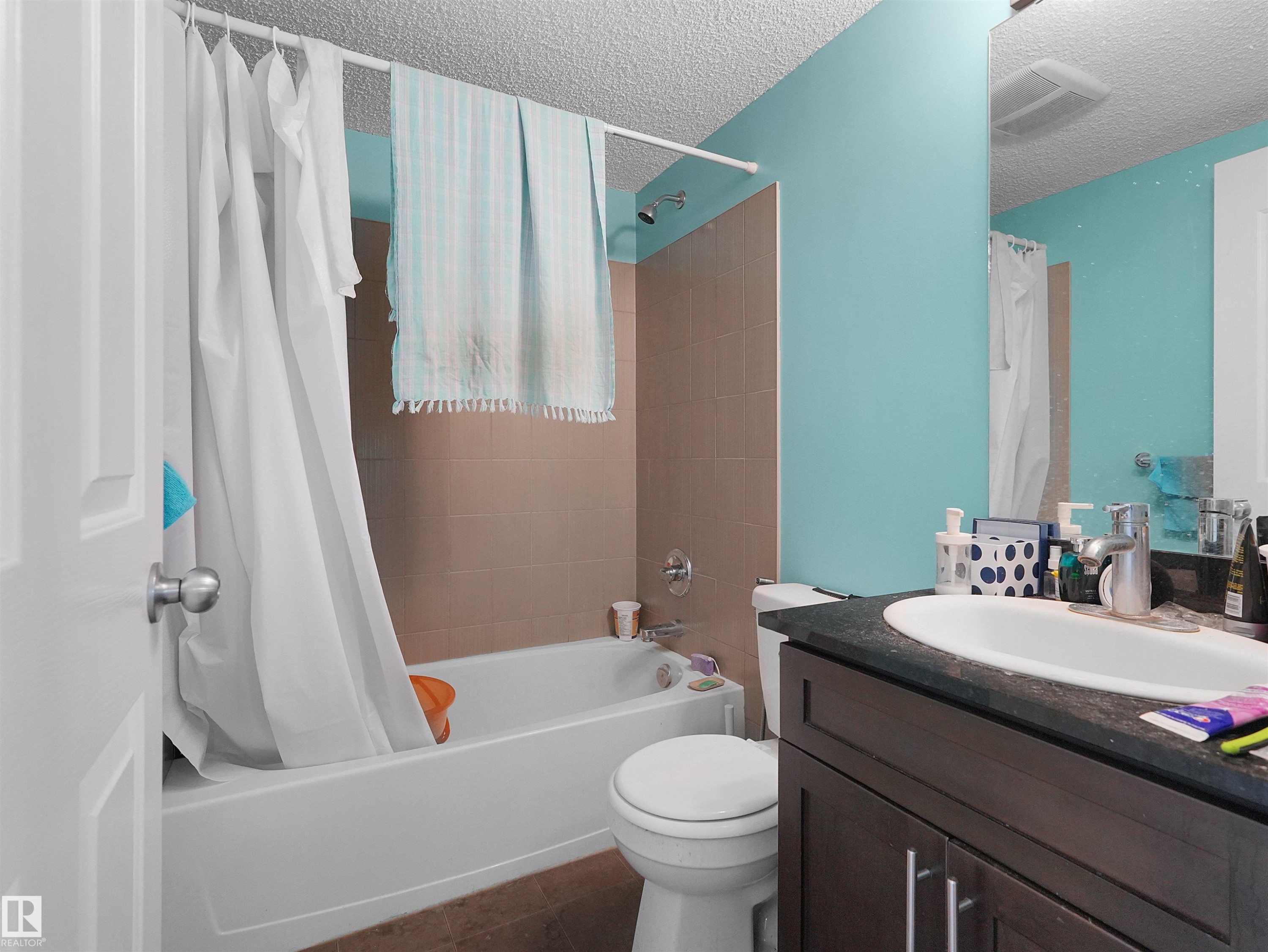 Full bathroom featuring a shower-tub combination with neutral-toned tiled surround, a dark wood-finish vanity with a built-in sink, and a large wall-mounted mirror - #313 11820 22 Av Sw, Edmonton, AB - Indoor Photo Showing Bathroom