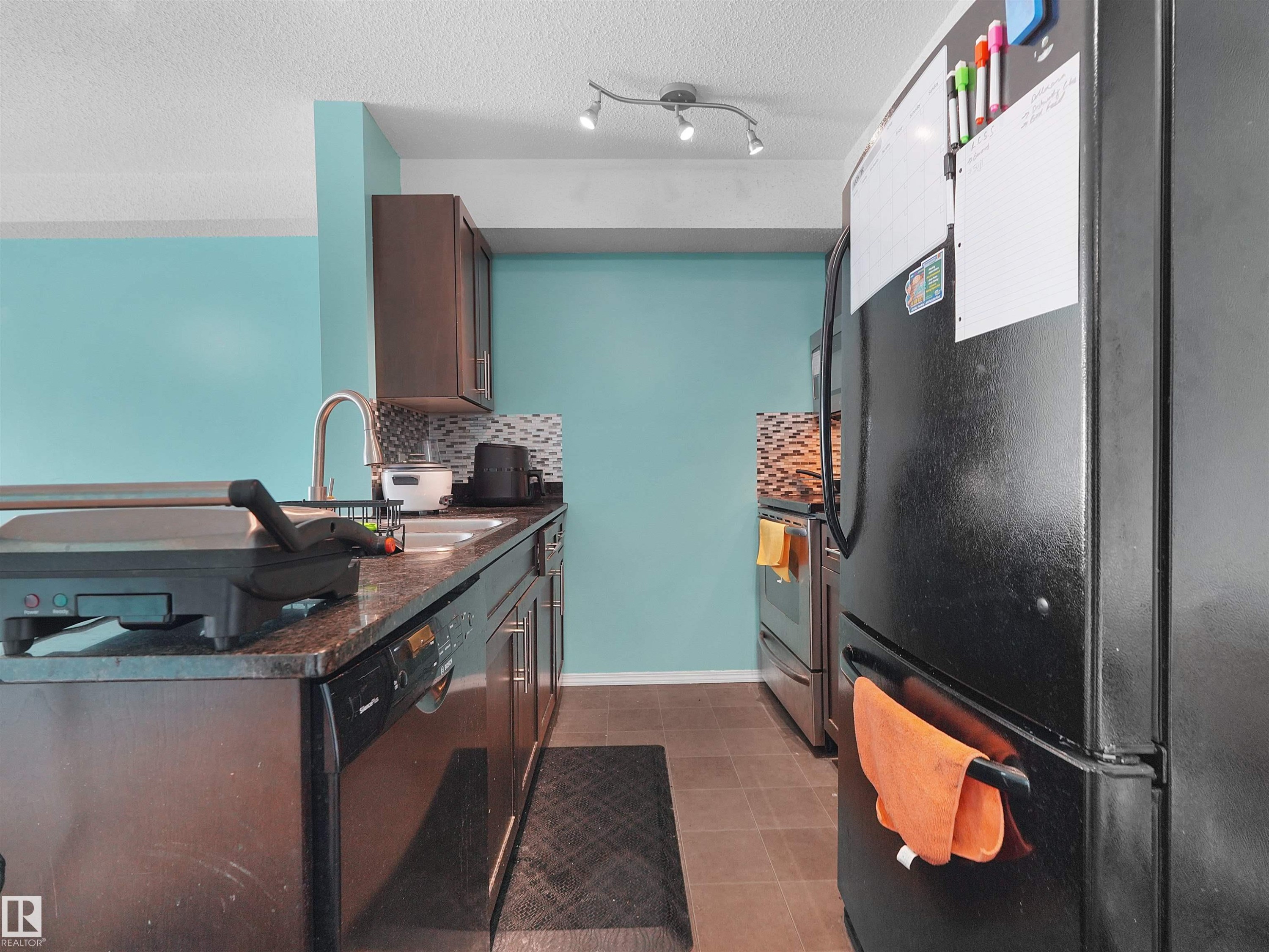Kitchen featuring dark cabinetry, granite-style countertops, and a tile backsplash - #313 11820 22 Av Sw, Edmonton, AB - Indoor Photo Showing Kitchen