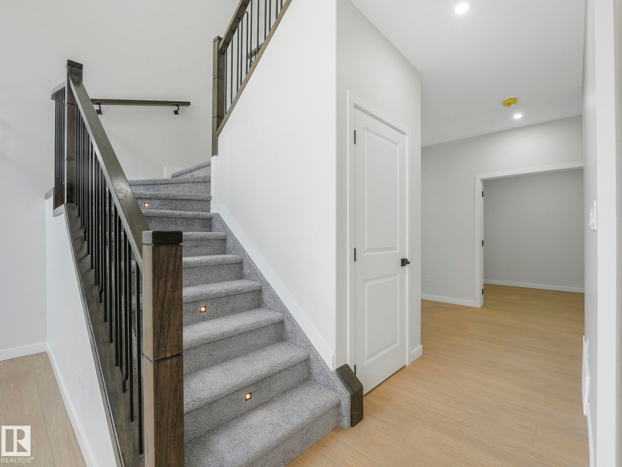 Staircase featuring dark wood newel posts and railings, black metal balusters, and gray carpeted treads with recessed lighting - 1717 Crossbill Loop, Edmonton, AB - Indoor Photo Showing Other Room