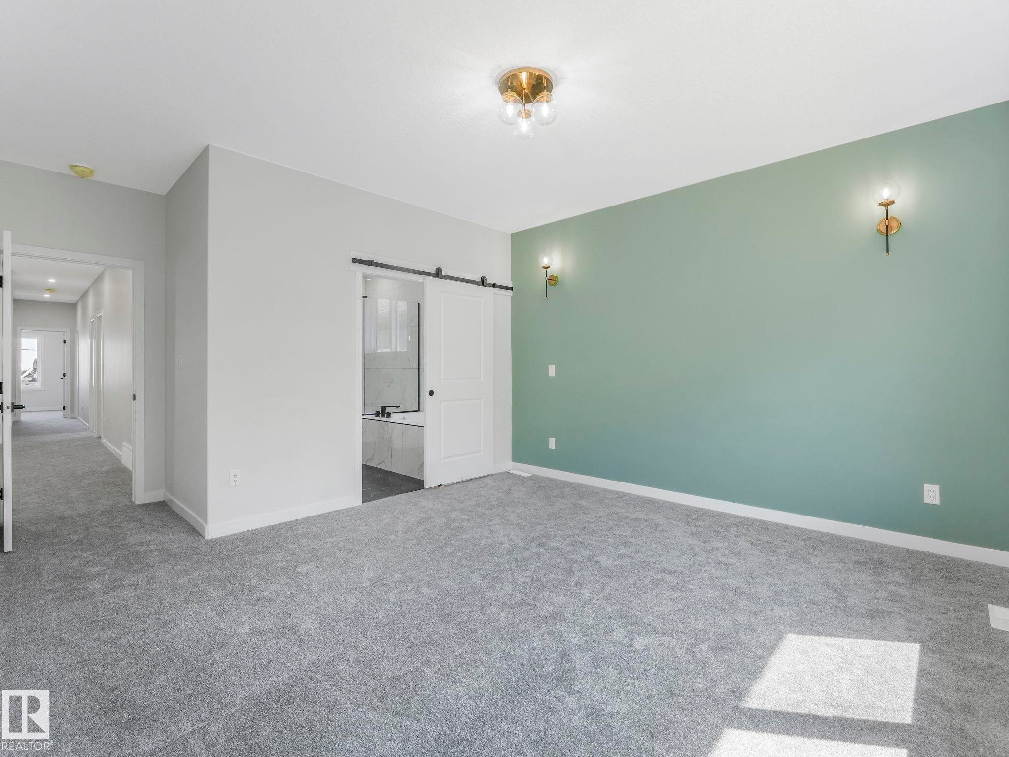 Spacious room featuring gray carpeting, a sage accent wall with sconce lighting, and a modern ceiling fixture - 1717 Crossbill Loop, Edmonton, AB - Indoor Photo Showing Other Room