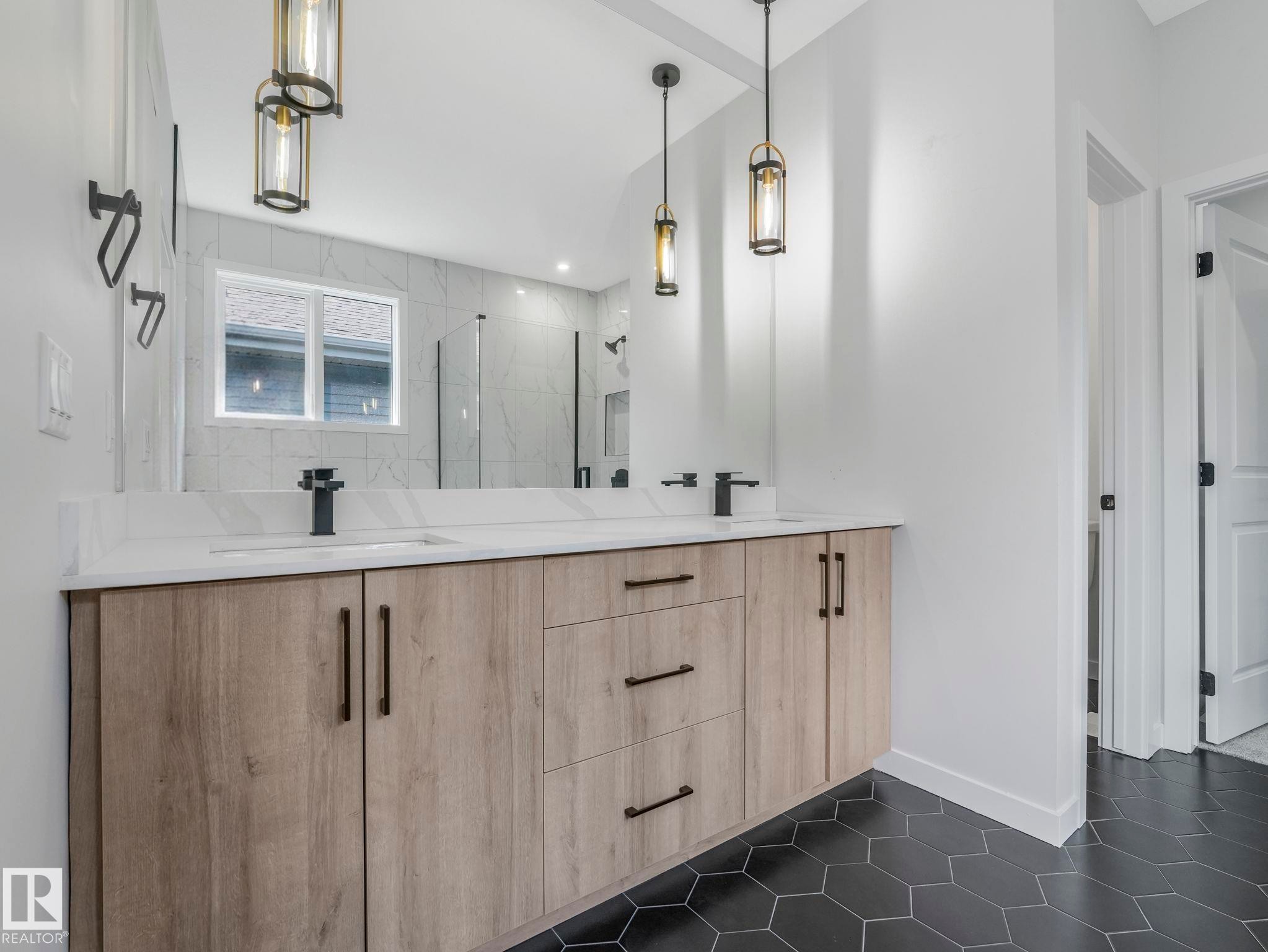 Double vanity with a light wood-finish cabinet, white countertop, and matte black fixtures - 1717 Crossbill Loop, Edmonton, AB - Indoor Photo Showing Bathroom