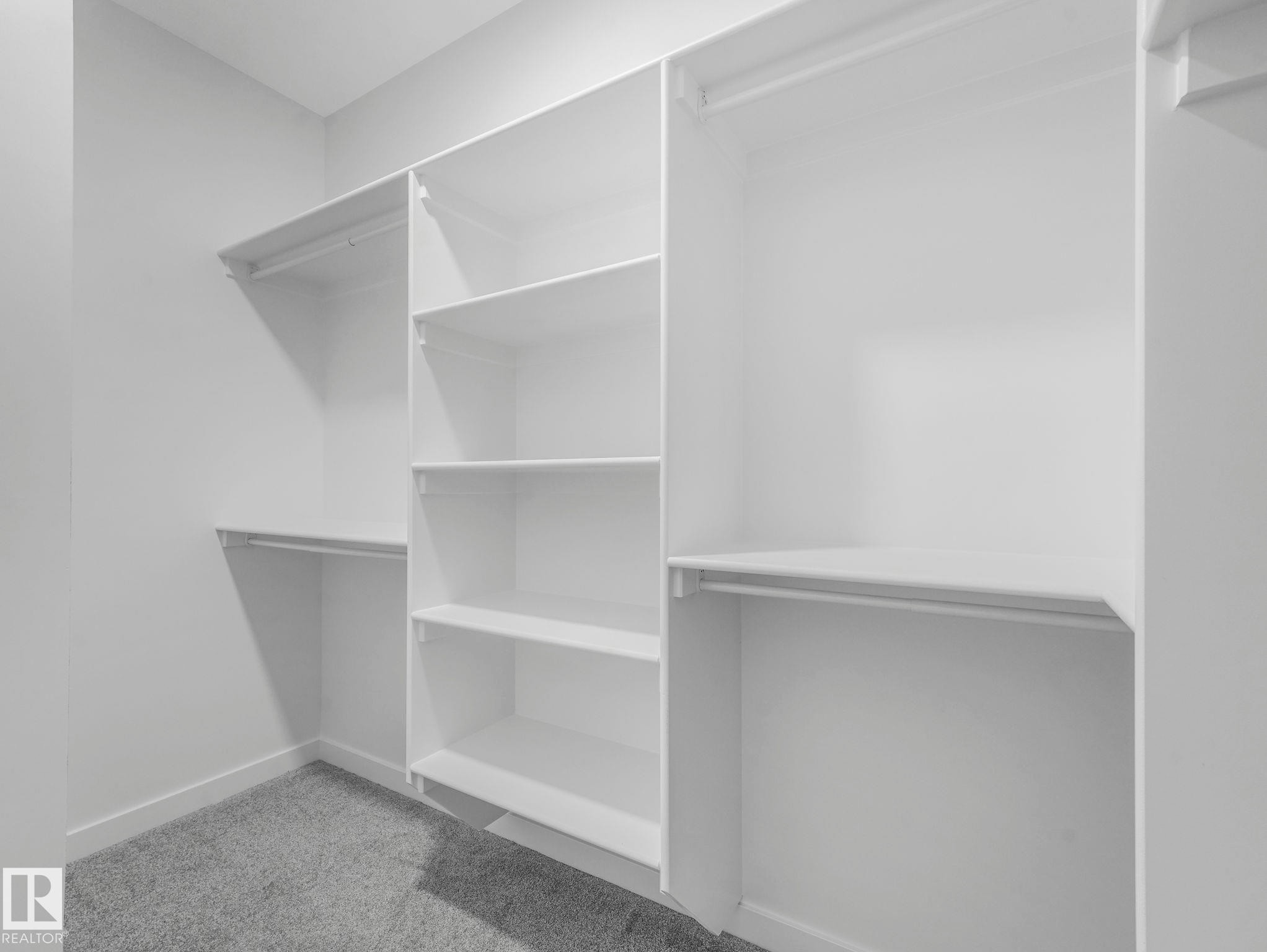 Expansive walk-in closet featuring white built-in shelving, multiple hanging rods, and light gray carpeting - 1717 Crossbill Loop, Edmonton, AB - Indoor With Storage