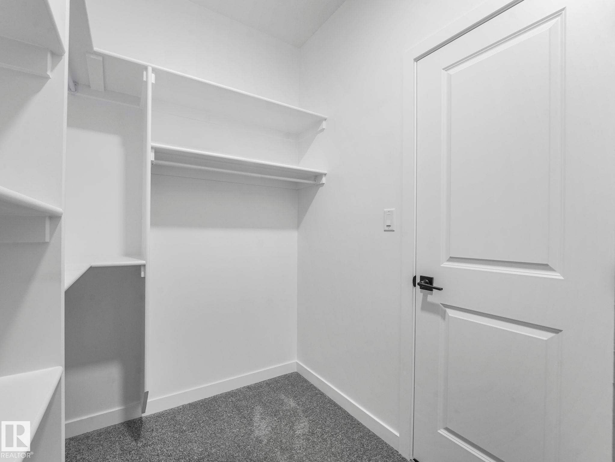Walk-in closet featuring white built-in shelving, hanging rods, and grey carpeting - 1717 Crossbill Loop, Edmonton, AB - Indoor With Storage