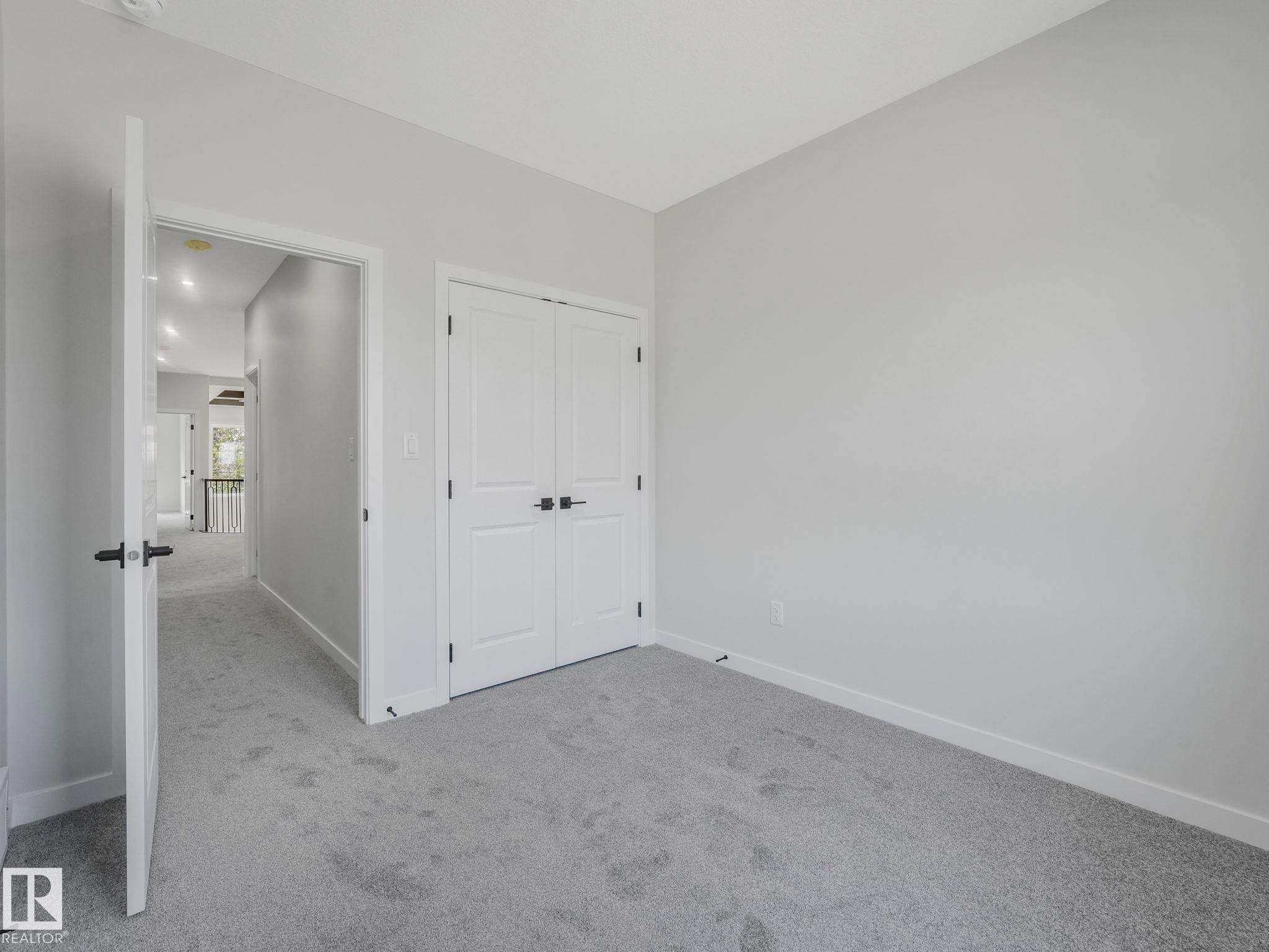 Carpeted interior room featuring light gray walls, white trim, and a double-door closet with dark hardware - 1717 Crossbill Loop, Edmonton, AB - Indoor Photo Showing Other Room