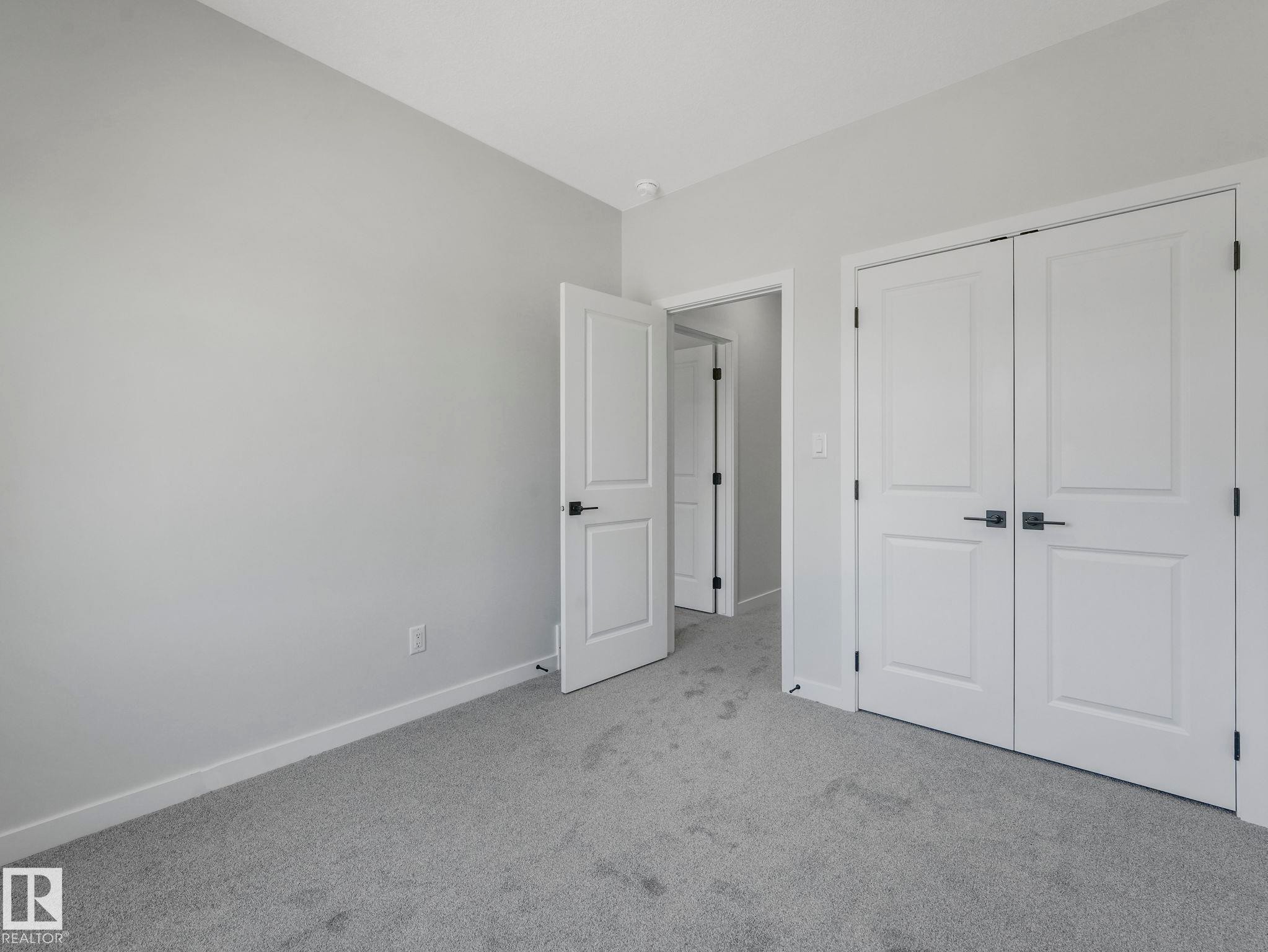 Light grey carpeted room featuring white trim, two panel doors with matte black hardware, and an additional doorway revealing a separate space - 1717 Crossbill Loop, Edmonton, AB - Indoor