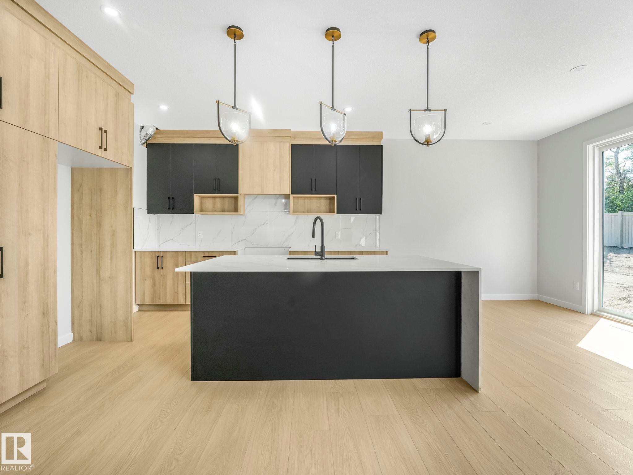 Kitchen featuring a large island with a waterfall countertop, light wood-finish flooring, two-tone cabinetry, marble-style backsplash, and three pendant lights - 1717 Crossbill Loop, Edmonton, AB - Indoor Photo Showing Kitchen With Upgraded Kitchen