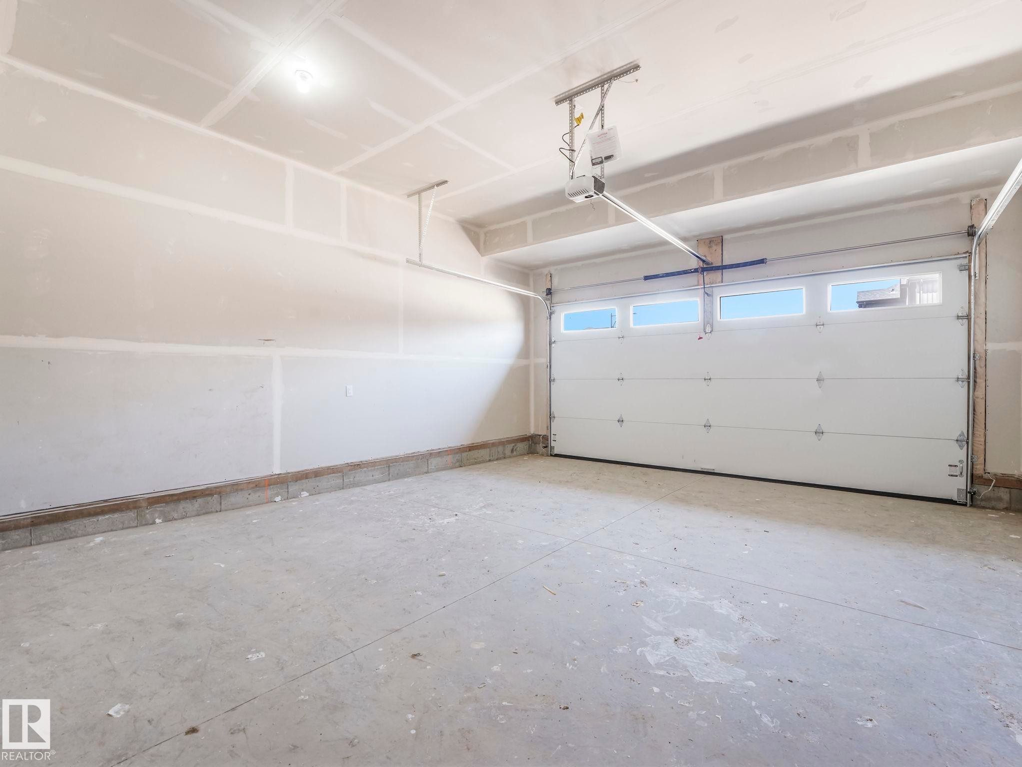 Spacious garage featuring a concrete floor, unpainted drywall, and a white paneled garage door with upper window inserts - 1717 Crossbill Loop, Edmonton, AB - Indoor Photo Showing Garage