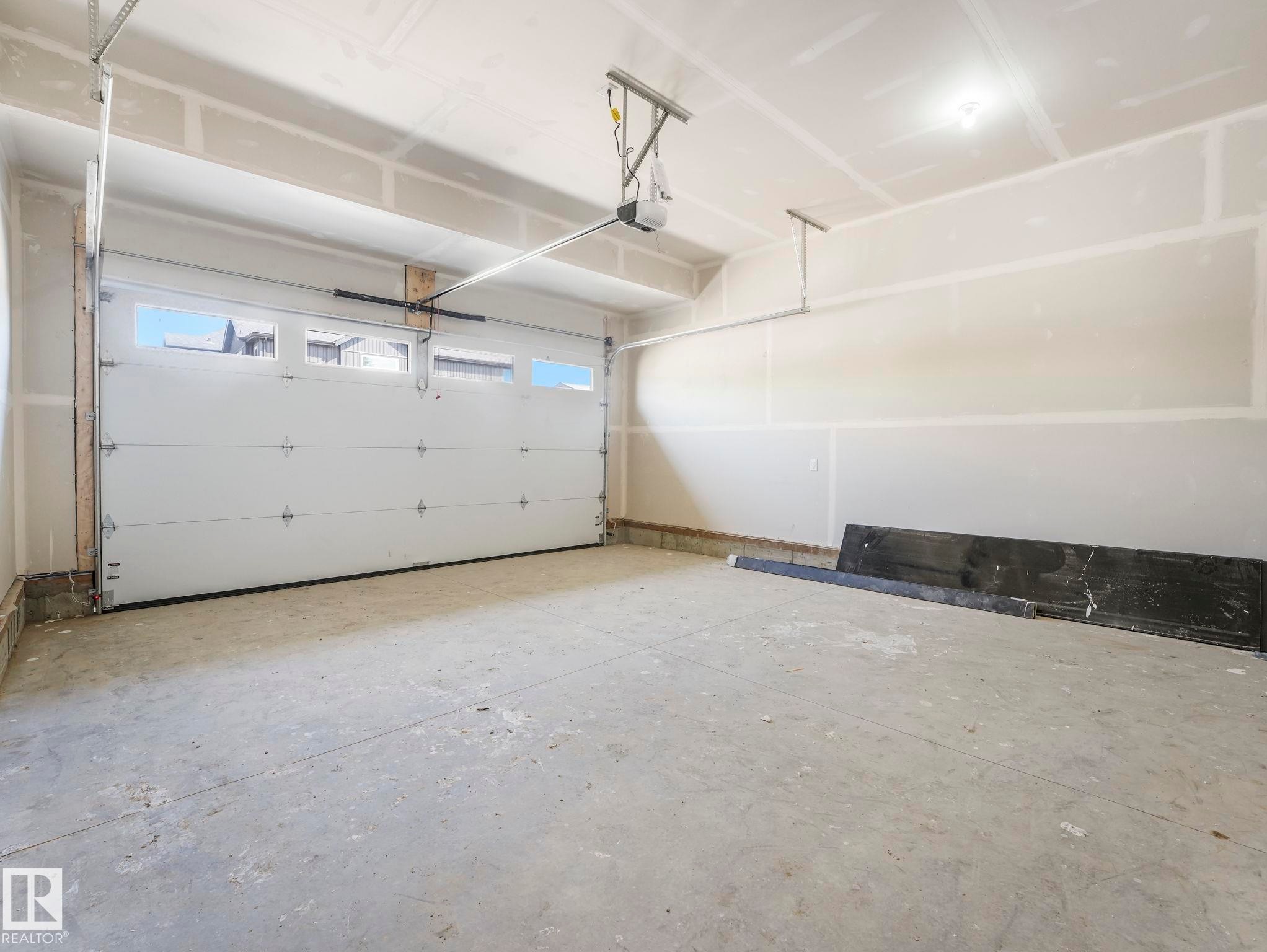 Spacious garage featuring a sectional overhead door with upper window panels, a concrete floor, and an automatic garage door opener - 1717 Crossbill Loop, Edmonton, AB - Indoor Photo Showing Garage