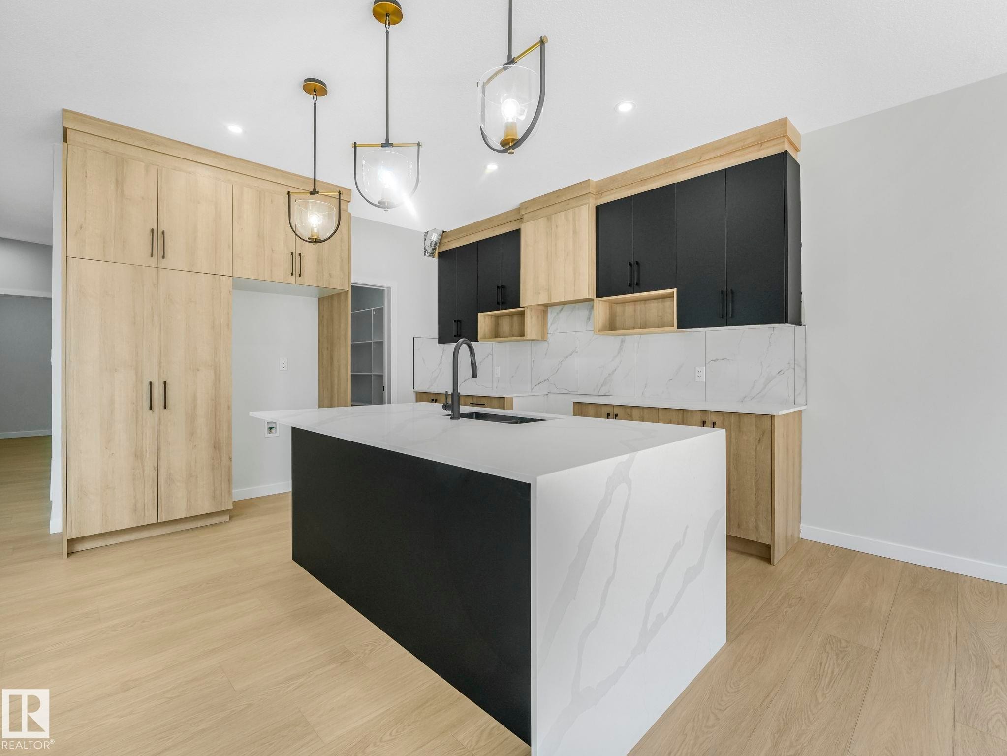 Modern kitchen featuring a large waterfall island with a white countertop and dark base, complemented by two pendant light fixtures - 1717 Crossbill Loop, Edmonton, AB - Indoor Photo Showing Kitchen With Upgraded Kitchen
