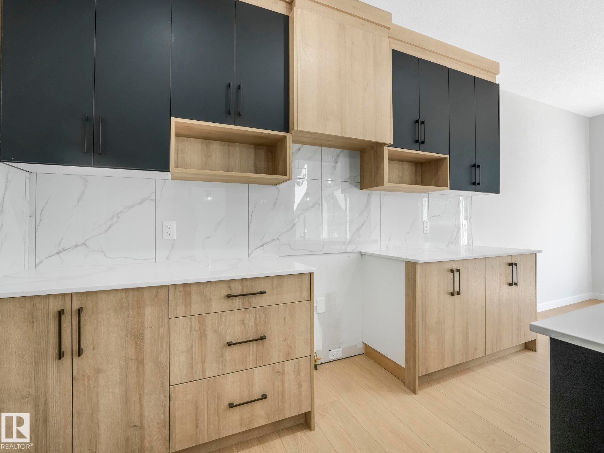 Modern kitchen featuring two-tone cabinetry with black and wood-finish doors, white countertops, a white marble-look tile backsplash, and light wood-finish flooring - 1717 Crossbill Loop, Edmonton, AB - Indoor Photo Showing Other Room