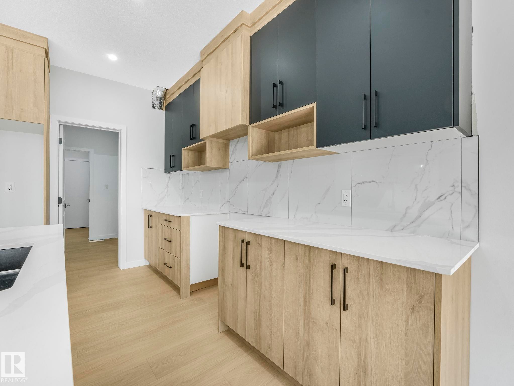 Modern kitchen featuring light wood-finish lower cabinetry, dark gray upper cabinetry with bronze hardware, and white countertops - 1717 Crossbill Loop, Edmonton, AB - Indoor Photo Showing Kitchen With Double Sink