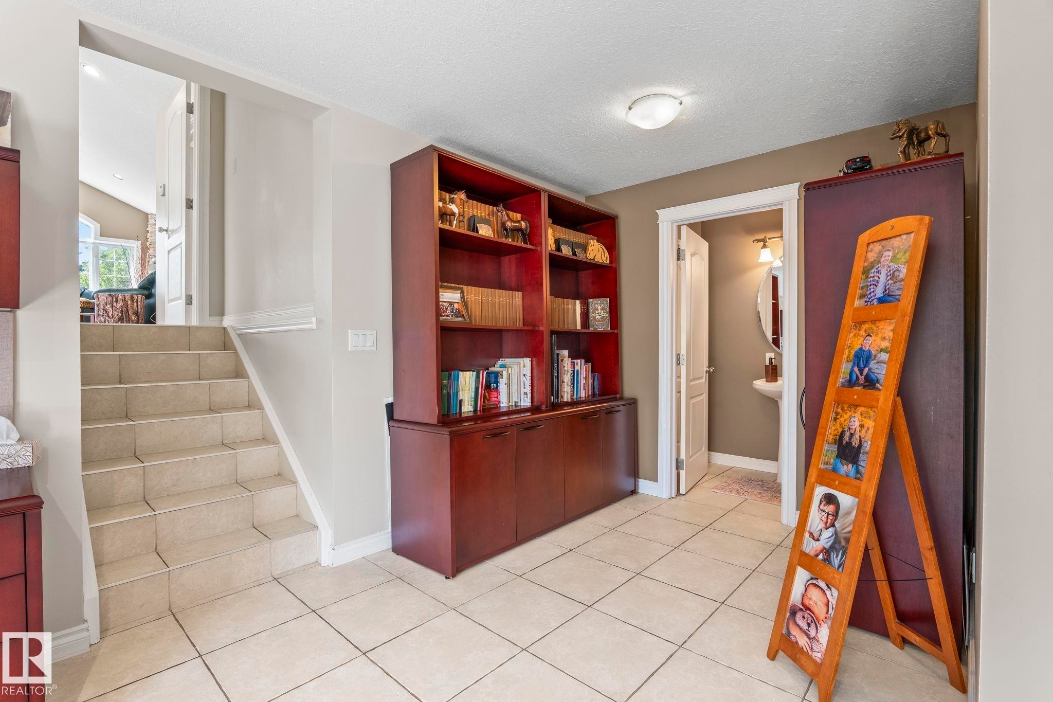 Tiled flooring extending to the staircase, built-in shelving unit with lower cabinetry, recessed lighting, and a partial view of a bathroom featuring a pedestal sink and oval mirror - 860 41 Avenue, Edmonton, AB