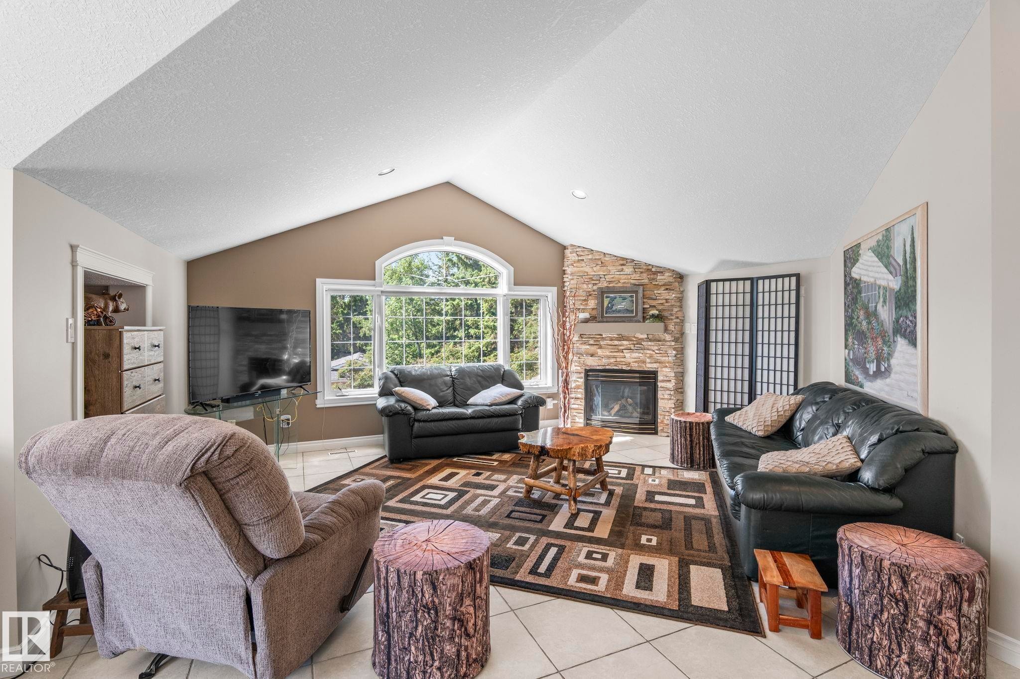 Vaulted ceiling living area featuring a stone-clad fireplace, large picture windows, arched transom window, and tile flooring - 860 41 Avenue, Edmonton, AB