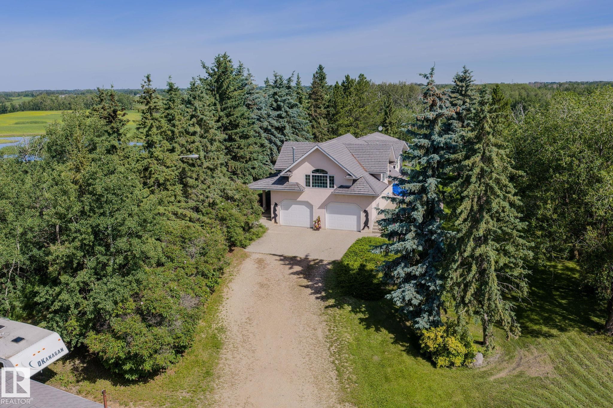 Stucco exterior residence featuring a multi-car garage, mature evergreen trees, expansive green space, and a paved driveway - 860 41 Avenue, Edmonton, AB
