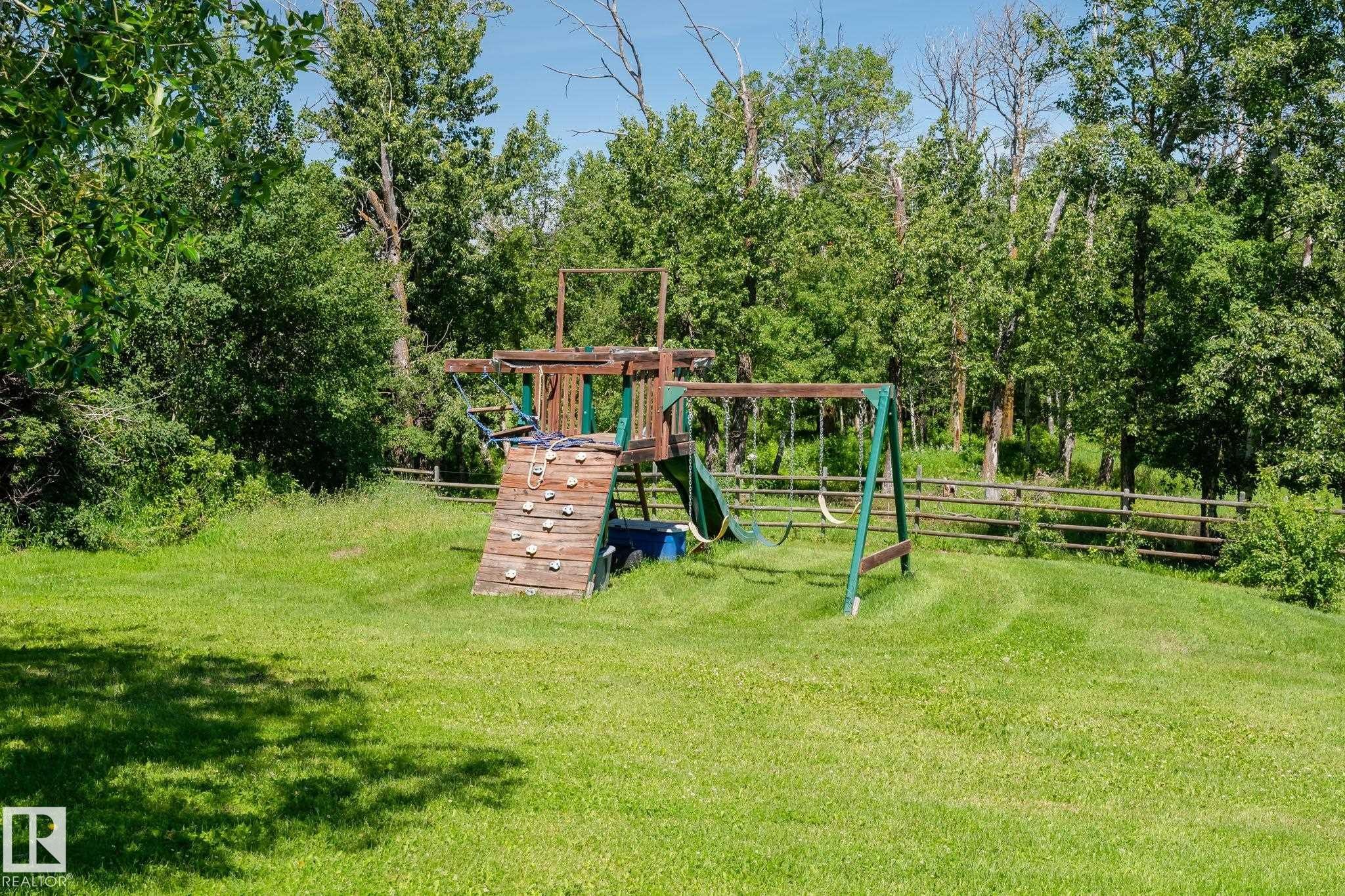 Expansive lawn area featuring a wooden playset with a climbing wall, slide, and swing set - 860 41 Avenue, Edmonton, AB