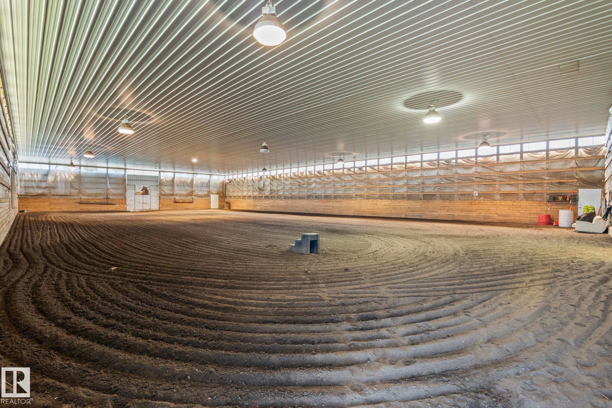 Spacious indoor arena featuring a corrugated metal ceiling, extensive lighting, and a prepared dirt surface with visible track patterns - 860 41 Avenue, Edmonton, AB