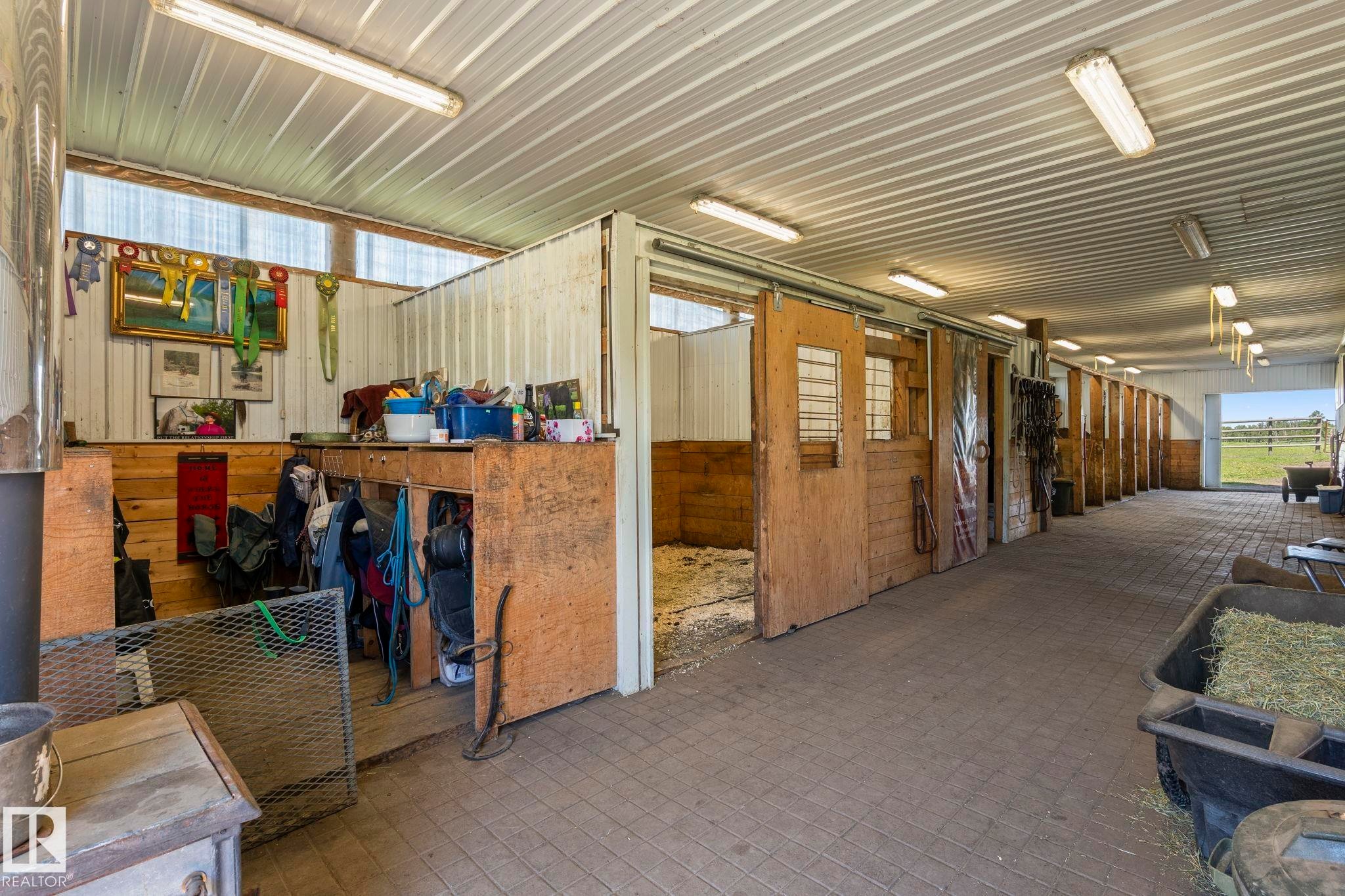 Barn interior featuring multiple stalls with sliding wood doors, a corrugated metal ceiling, and overhead fluorescent lighting - 860 41 Avenue, Edmonton, AB