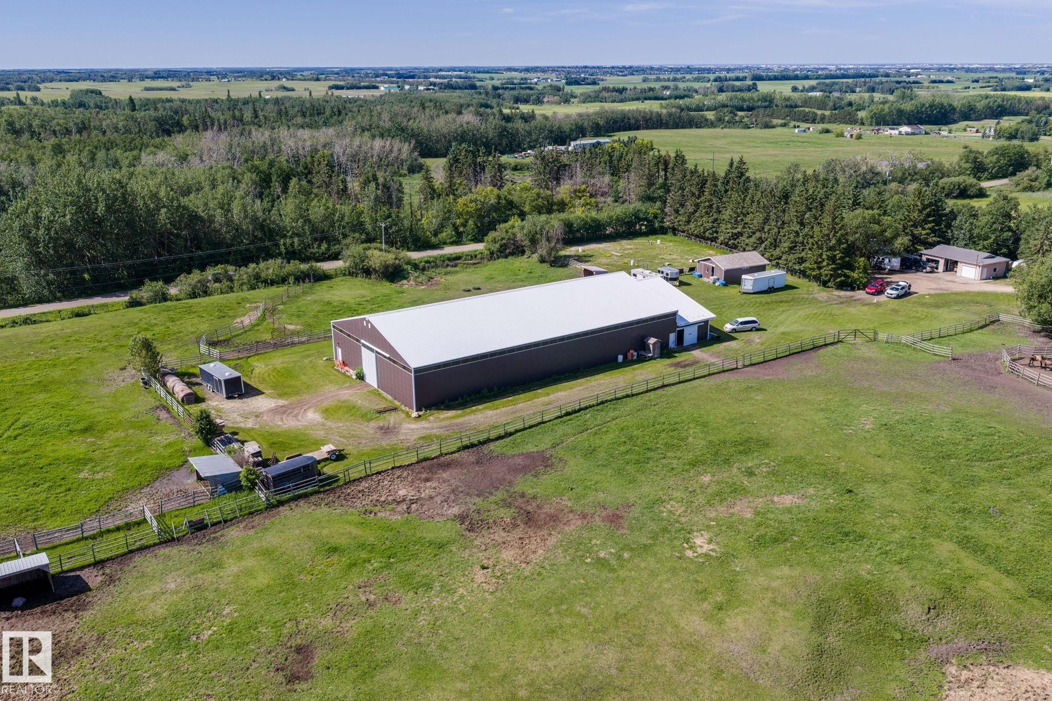 Expansive agricultural property featuring a large brown barn with a white roof, surrounded by green fields and mature trees - 860 41 Avenue, Edmonton, AB