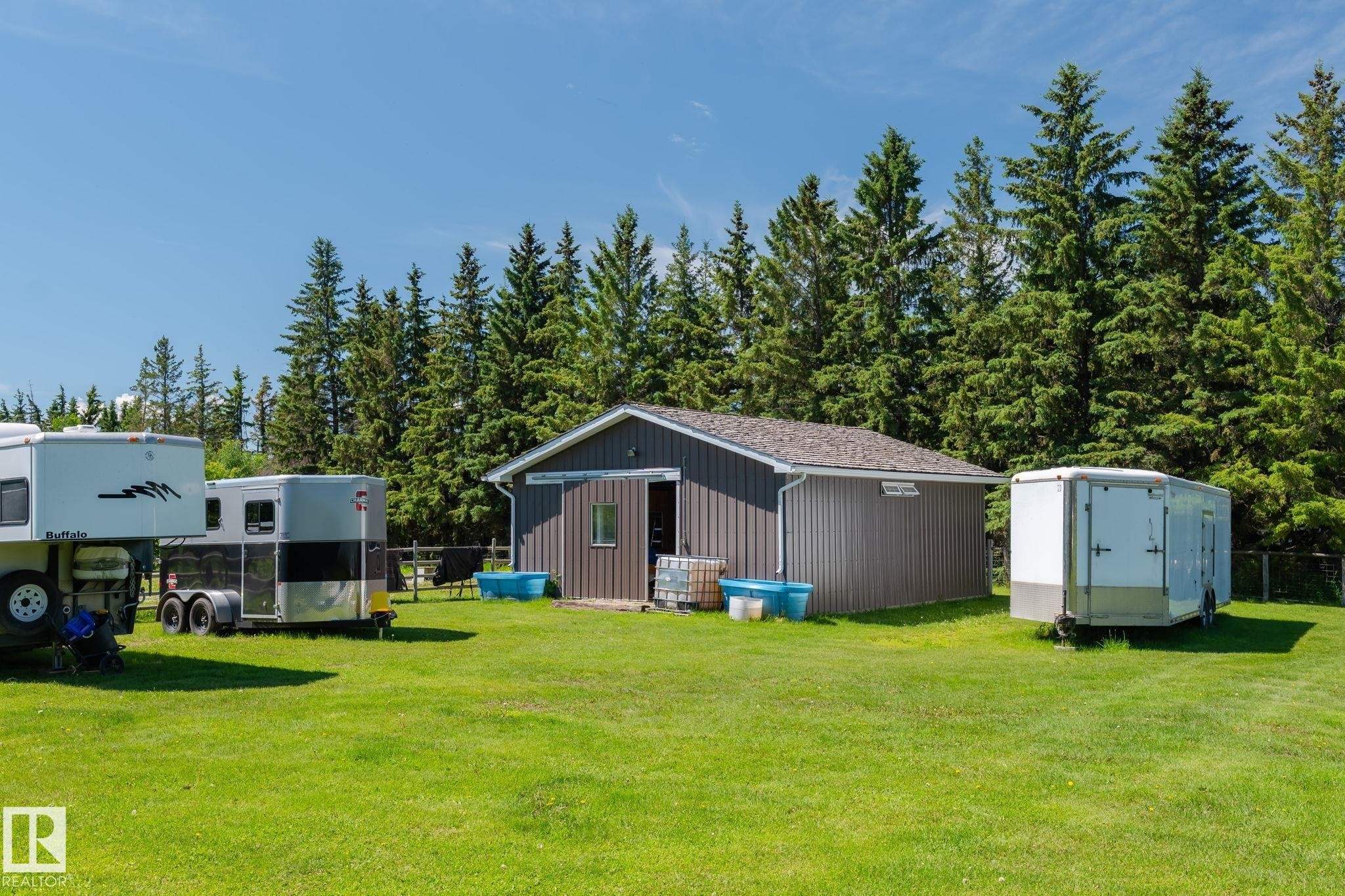 Outbuilding with brown vertical siding and a shingled roof, surrounded by expansive green lawn and mature evergreen trees - 860 41 Avenue, Edmonton, AB
