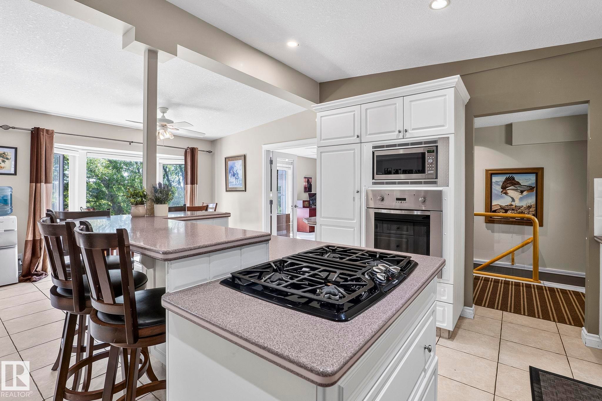 Kitchen featuring a gas cooktop on a central island, built-in stainless steel microwave and oven, white cabinetry, and light-toned countertops - 860 41 Avenue, Edmonton, AB