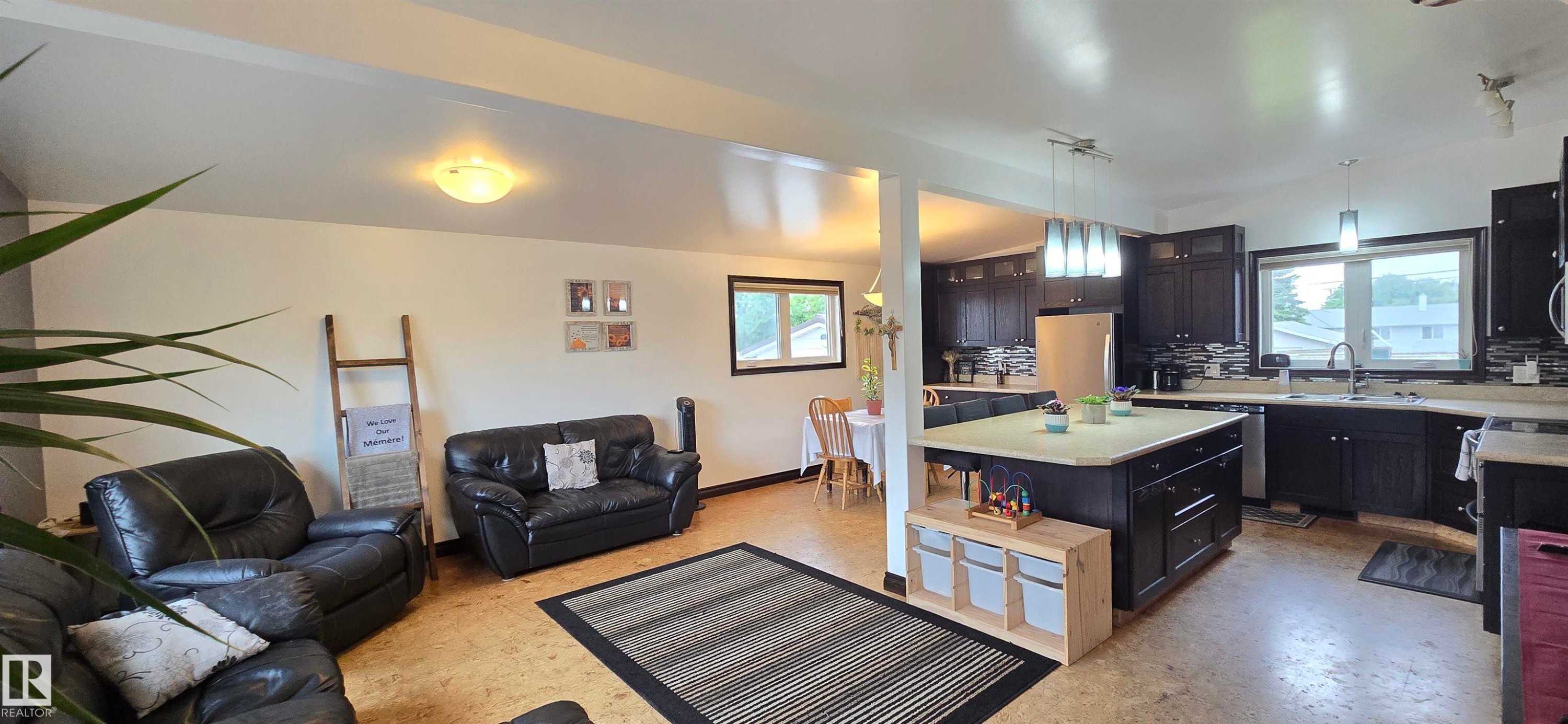 Open-concept living space featuring wood-finish flooring, a kitchen island with storage, dark wood cabinetry, a tiled backsplash, and recessed lighting - 5304 49 Street, Two Hills, AB - Indoor Photo Showing Living Room