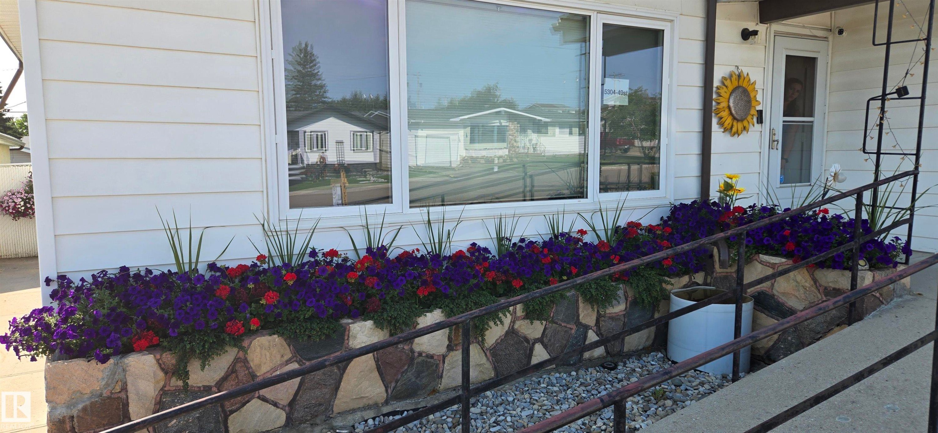 Front exterior featuring horizontal siding and a stone-clad planter with vibrant plantings - 5304 49 Street, Two Hills, AB - Outdoor With Exterior