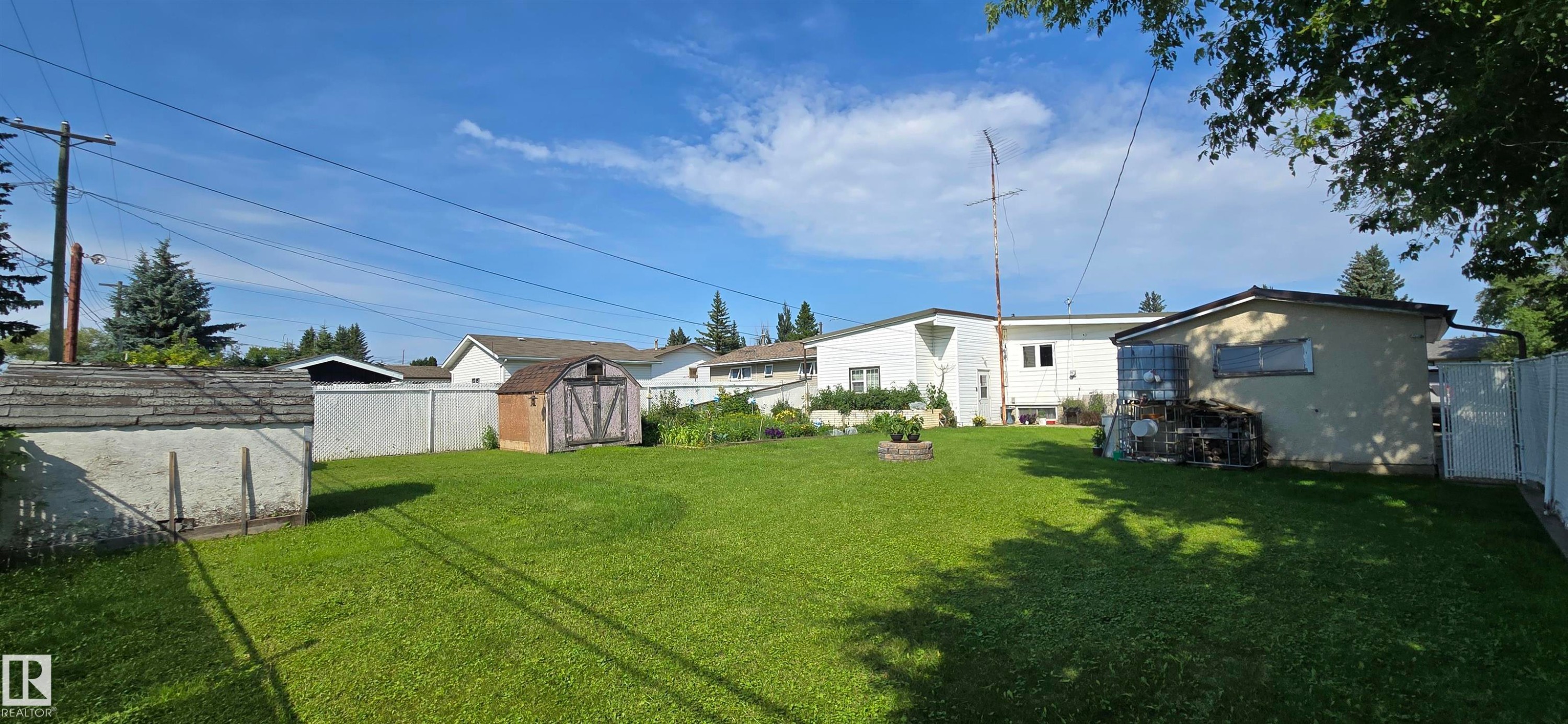 Spacious backyard featuring an expansive lawn, a detached storage shed with a gambrel roof, and a second detached shed - 5304 49 Street, Two Hills, AB - Outdoor