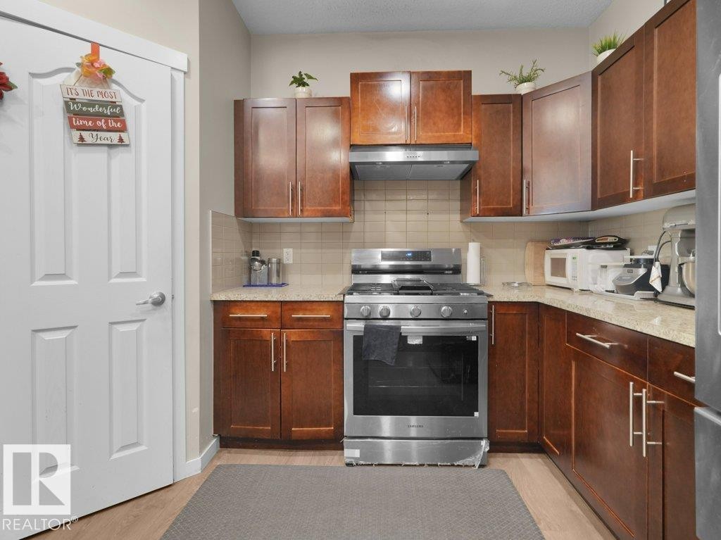 Kitchen featuring wood-finish cabinetry, stainless steel range and hood, light-toned countertops, and a tiled backsplash - 1419 27 Av, Edmonton, AB