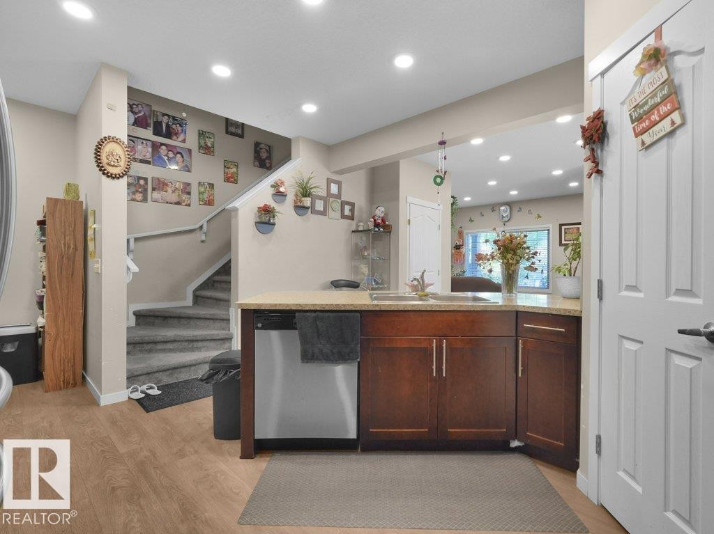 Kitchen peninsula featuring wood-finish cabinetry, light-toned countertop, and stainless steel dishwasher - 1419 27 Av, Edmonton, AB