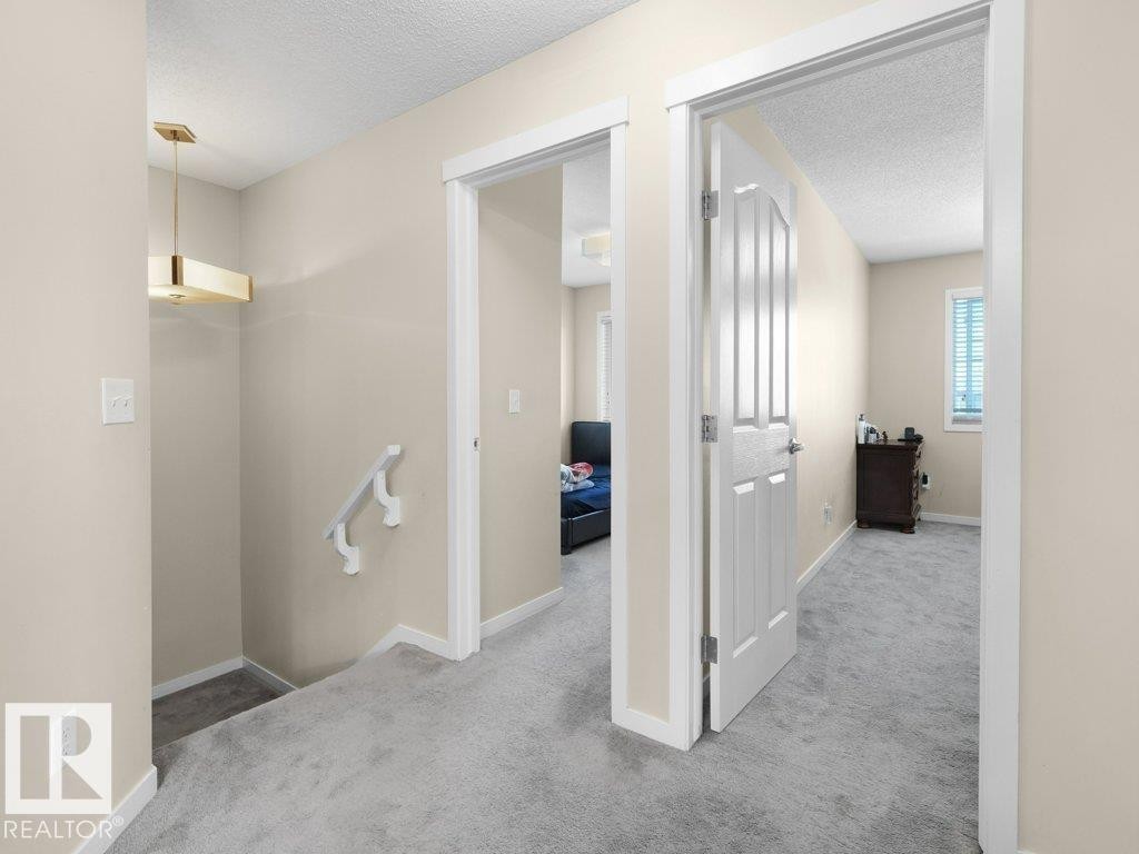 Upper-level hallway featuring neutral wall paint, light gray carpet, white trim, and a modern gold-tone ceiling fixture - 1419 27 Av, Edmonton, AB