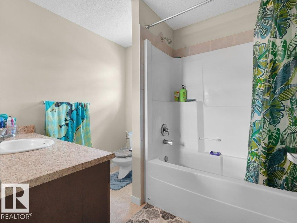 White bathtub and shower combination unit featuring a built-in shelf and chrome fixtures, complemented by a light-toned wall tile accent - 1419 27 Av, Edmonton, AB