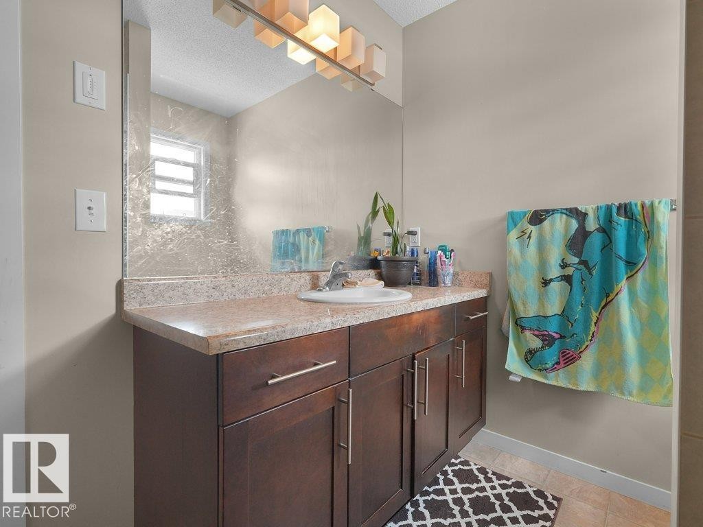 Vanity featuring wood-finish cabinetry with brushed nickel hardware, a speckled countertop, and an integrated white sink - 1419 27 Av, Edmonton, AB