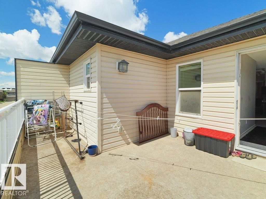Outdoor concrete patio with light-colored siding, a white railing, and an exterior light fixture - 1419 27 Av, Edmonton, AB