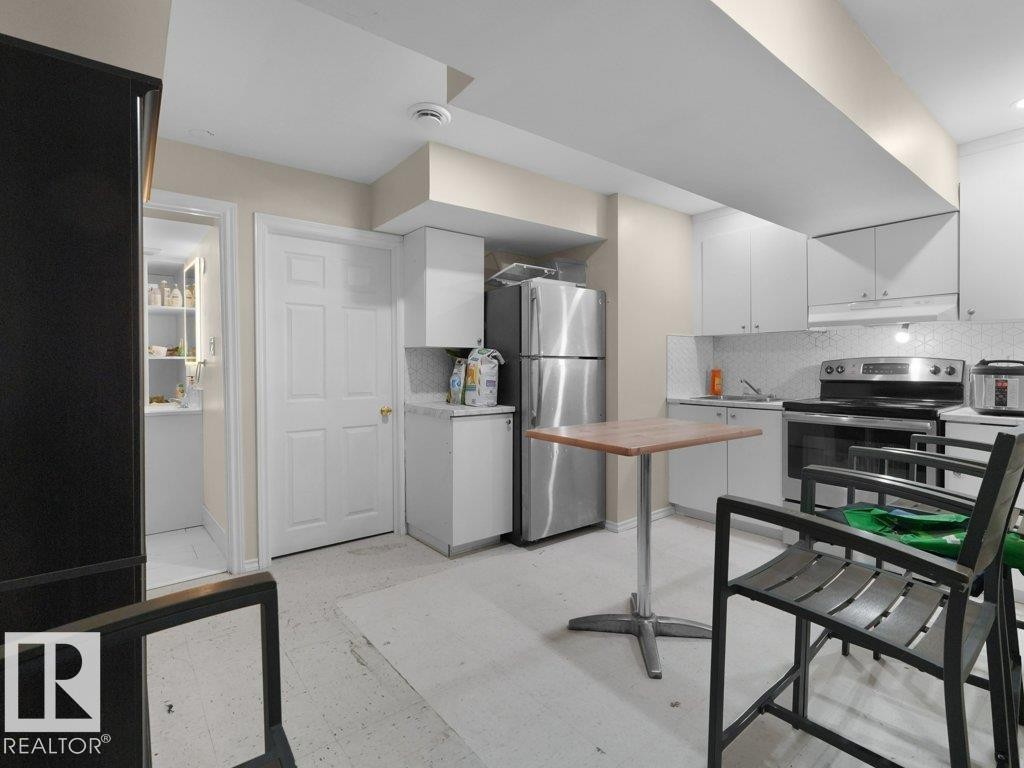 Kitchen featuring stainless steel appliances, white cabinetry, and a tile backsplash - 1419 27 Av, Edmonton, AB