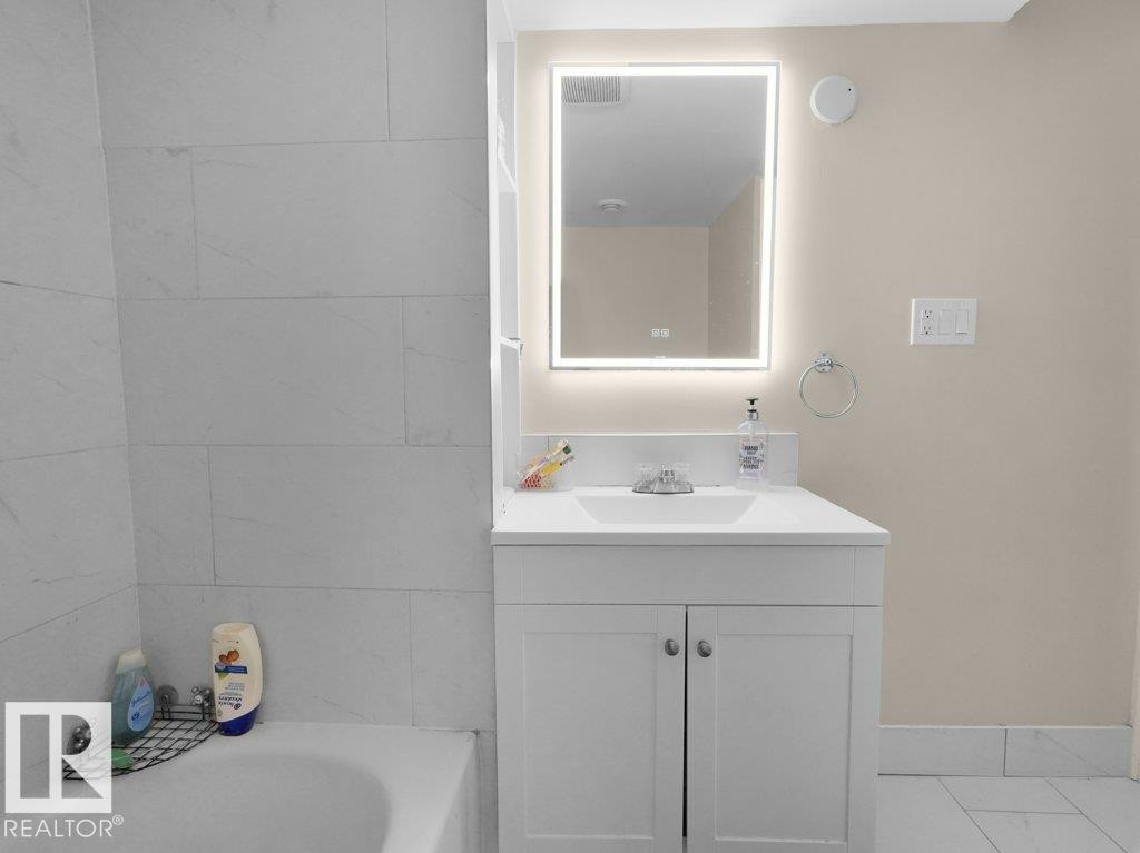 Bathroom vanity featuring a vessel sink, integrated LED mirror, and white cabinetry - 1419 27 Av, Edmonton, AB
