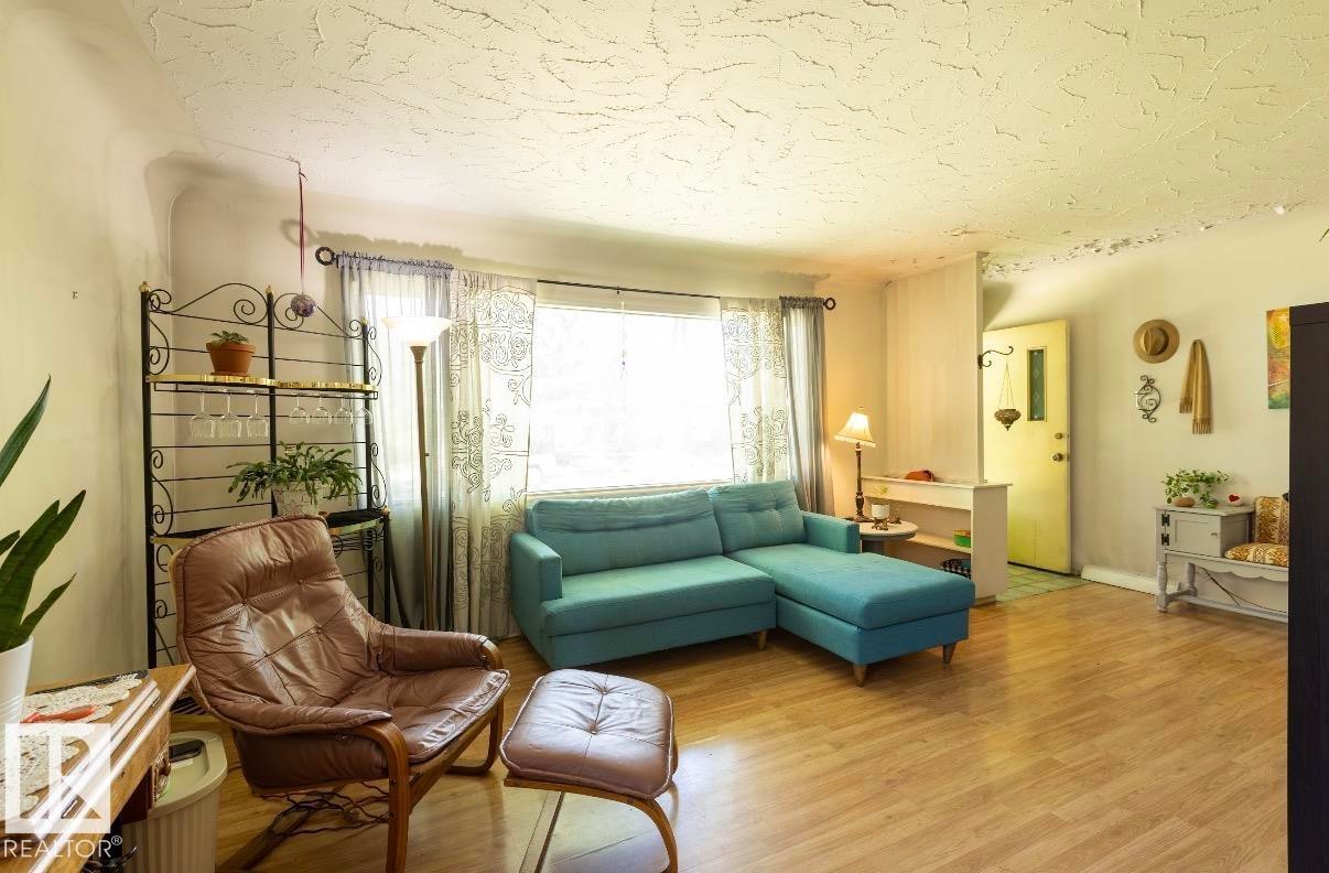 Spacious living area featuring light wood-finish flooring and a large window with sheer curtains - 8719 67 Avenue Nw, Edmonton, AB - Indoor Photo Showing Living Room