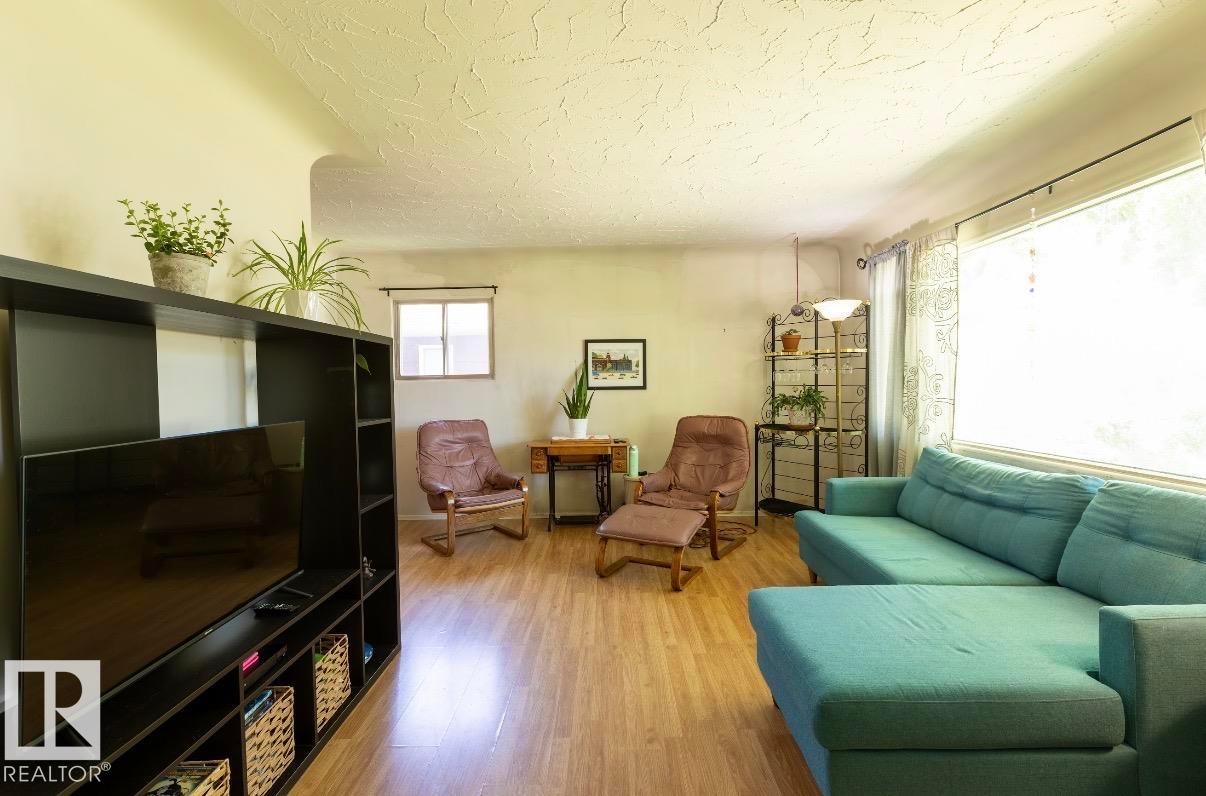 Interior space featuring wood-finish flooring, textured ceilings, and a large window with roller shades - 8719 67 Avenue Nw, Edmonton, AB - Indoor Photo Showing Living Room