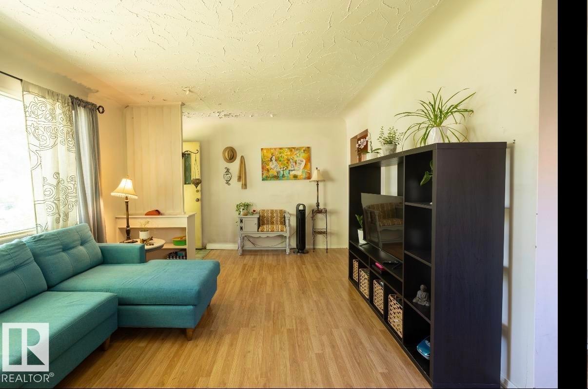Expansive living area featuring wood-finish flooring, light-toned walls, and a large window with sheer and blackout curtains - 8719 67 Avenue Nw, Edmonton, AB - Indoor Photo Showing Living Room