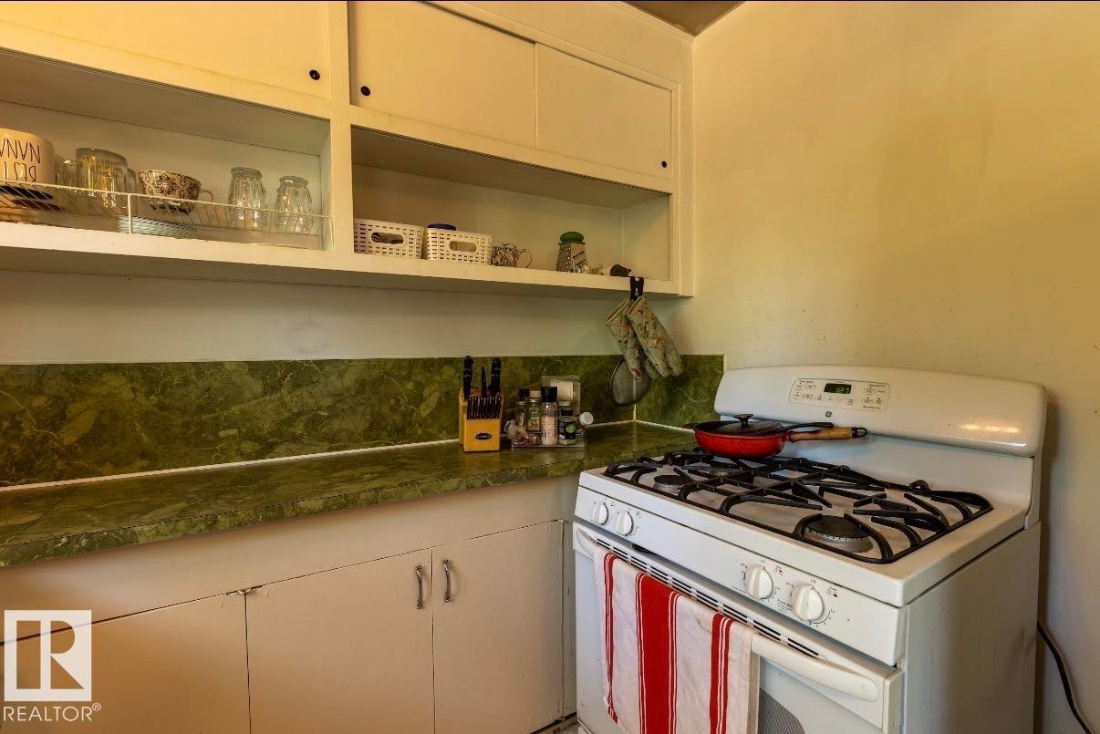 Kitchen featuring a white gas range, green patterned countertops, matching backsplash, and upper and lower cabinetry - 8719 67 Avenue Nw, Edmonton, AB - Indoor Photo Showing Kitchen