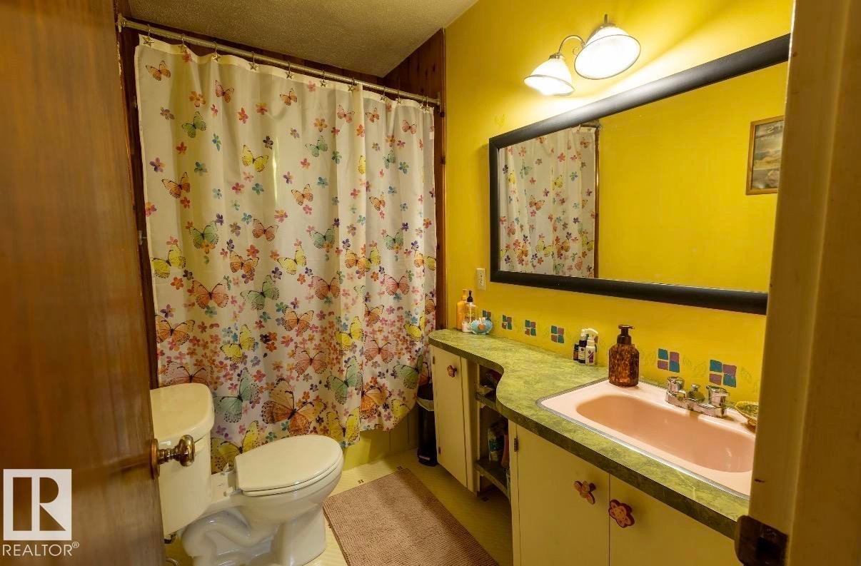 Bathroom featuring a built-in vanity with a pink basin and green countertop, a white toilet, and a framed wall mirror with integrated lighting - 8719 67 Avenue Nw, Edmonton, AB - Indoor Photo Showing Bathroom