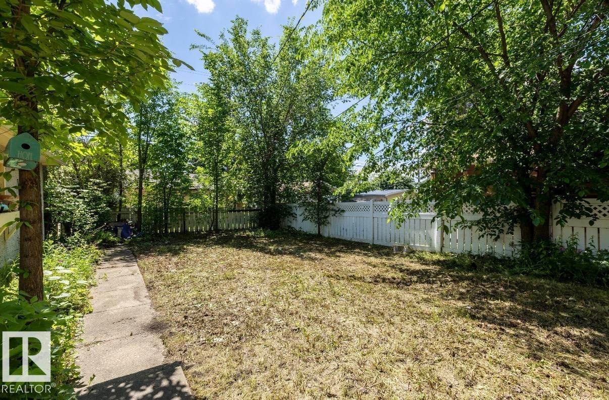 Spacious backyard featuring a rectangular lawn area, mature trees, and a white picket fence - 8719 67 Avenue Nw, Edmonton, AB - Outdoor