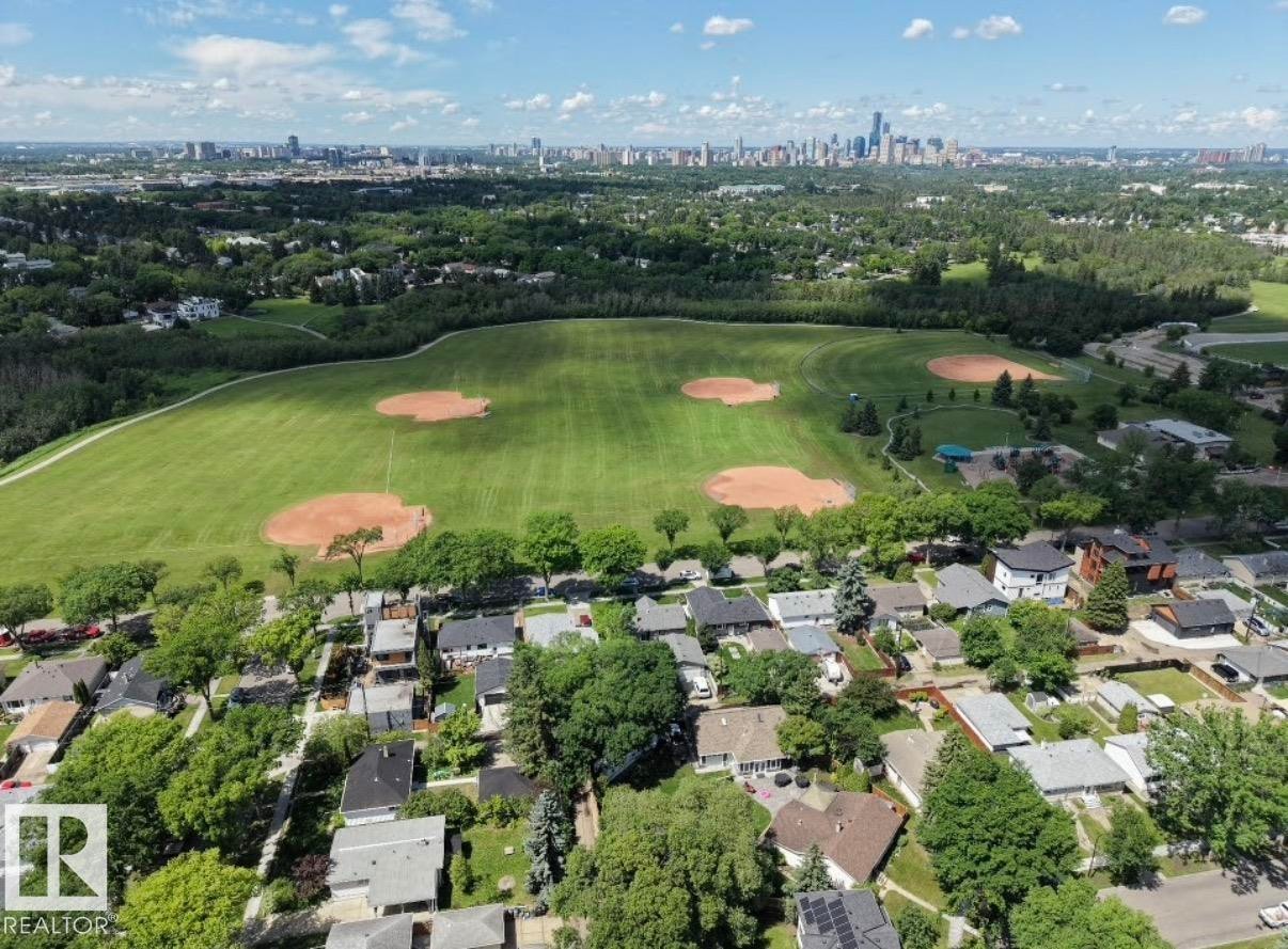 Aerial perspective showcasing a residential neighborhood with varied roofing materials, mature tree canopy, and green spaces featuring multiple baseball diamonds - 8719 67 Avenue Nw, Edmonton, AB - Outdoor With View