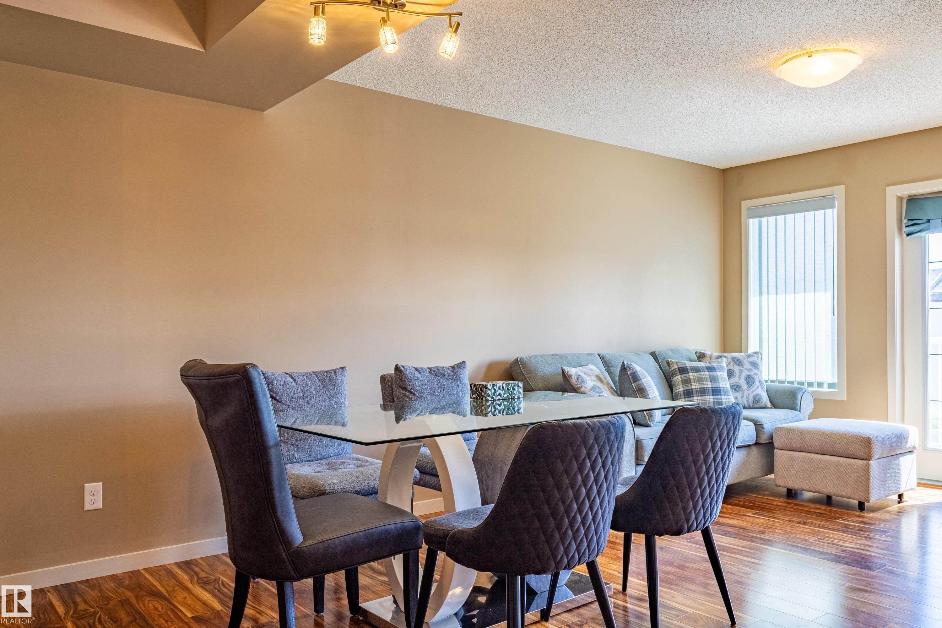 Open concept dining space featuring wood-finish flooring, a modern ceiling light fixture, and neutral wall tones - 13 1816 Rutherford Road, Edmonton, AB
