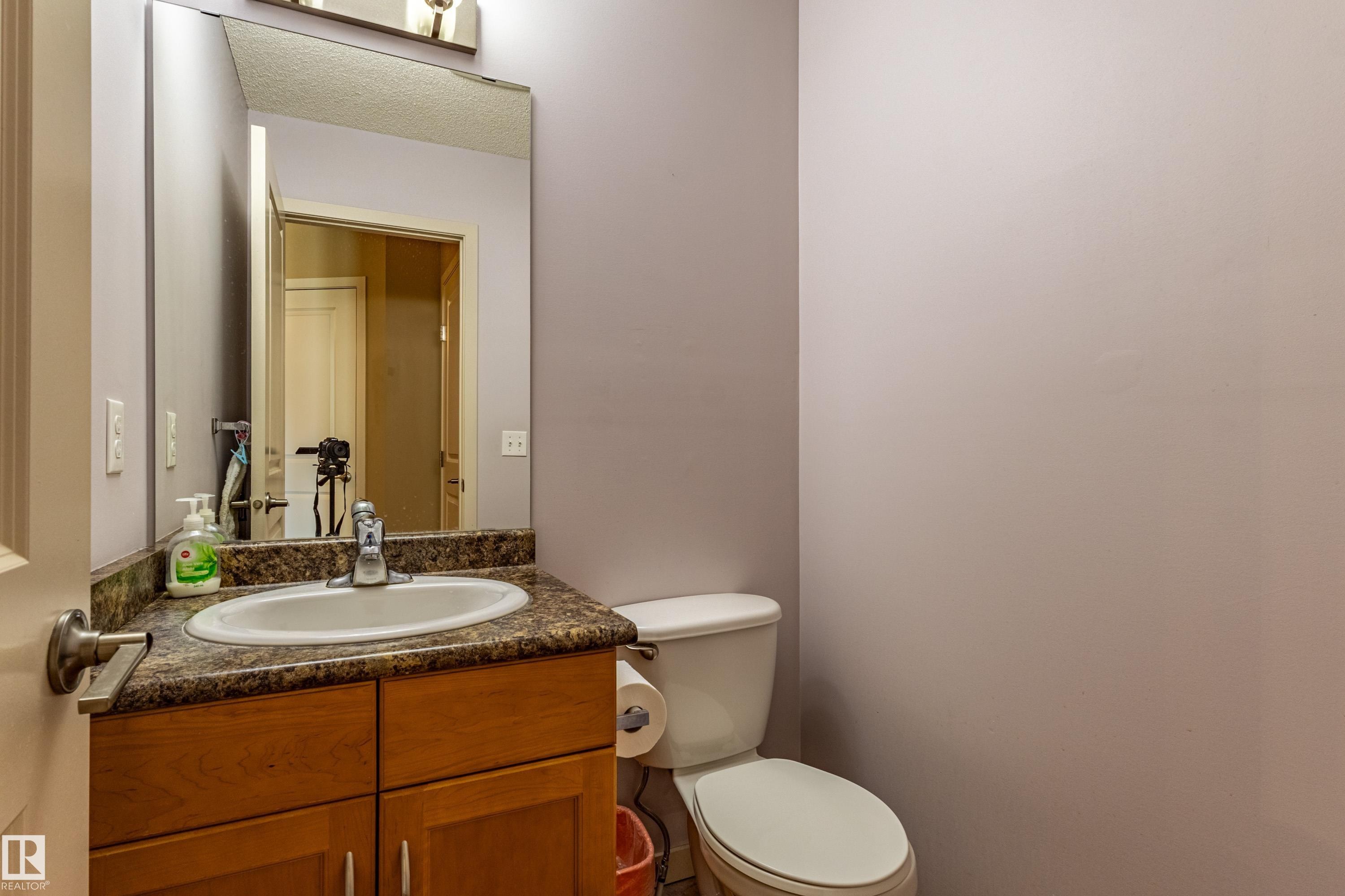 Vanity with wood-finish cabinetry, a stone-finish countertop, and an integrated white oval sink - 13 1816 Rutherford Road, Edmonton, AB