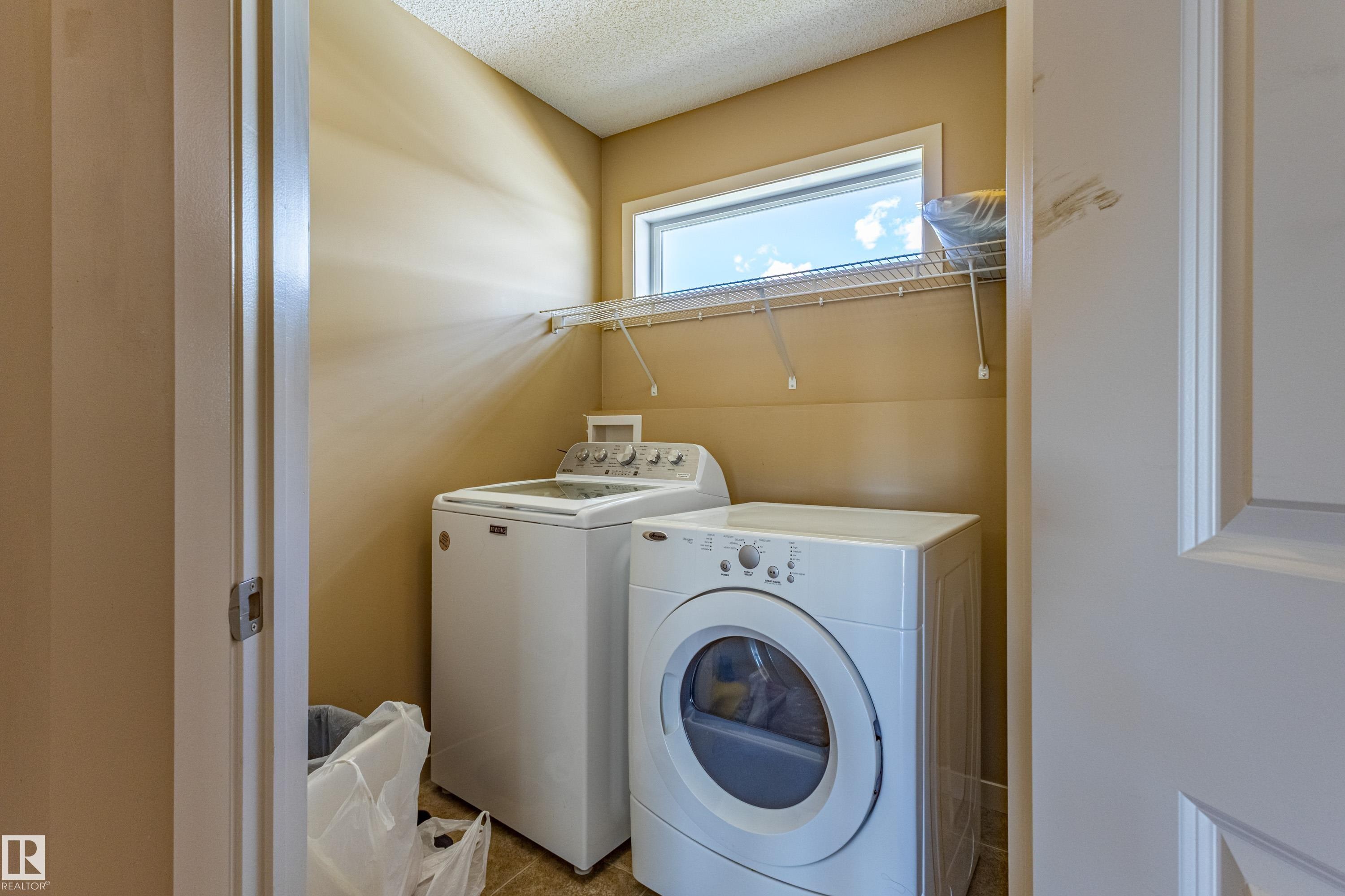 Dedicated laundry area featuring a horizontal window, wall-mounted wire shelving, and neutral wall paint - 13 1816 Rutherford Road, Edmonton, AB