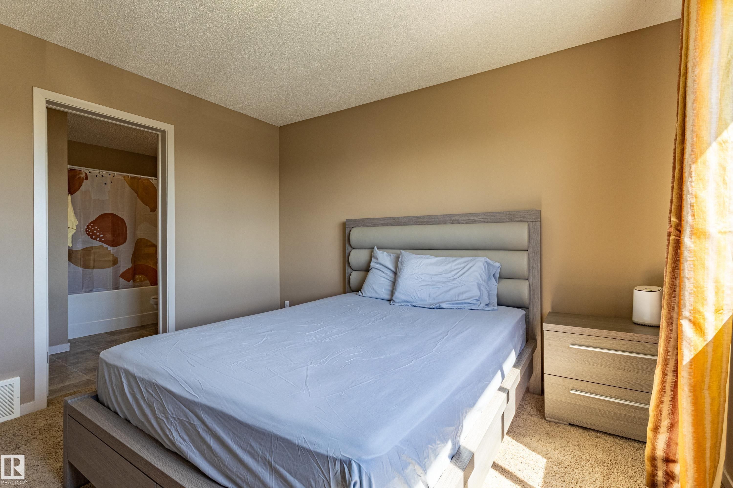 Carpeted room featuring a neutral color palette, an entryway to a bathroom with a white bathtub, and a window with natural light - 13 1816 Rutherford Road, Edmonton, AB