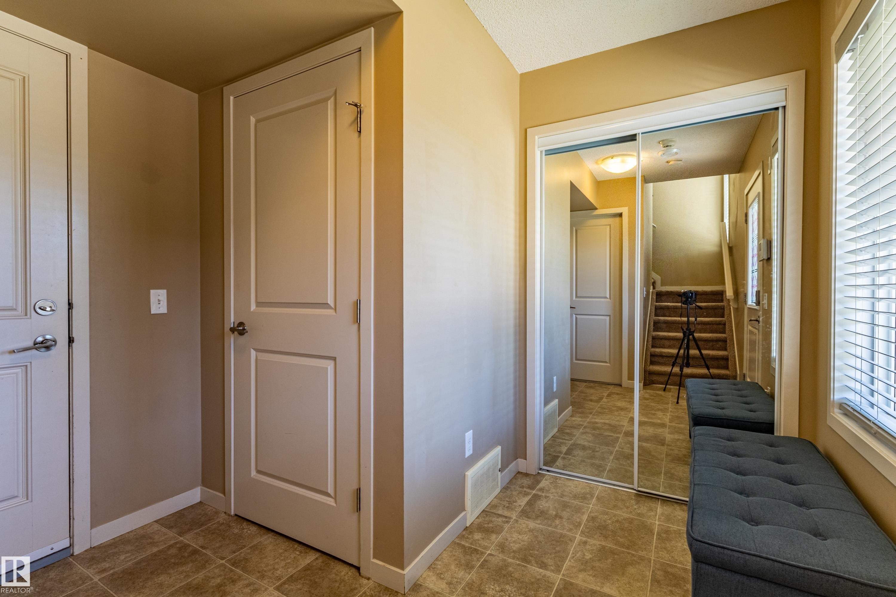 Entryway featuring tile flooring, neutral wall tones, white trim, and a full-height mirrored closet - 13 1816 Rutherford Road, Edmonton, AB