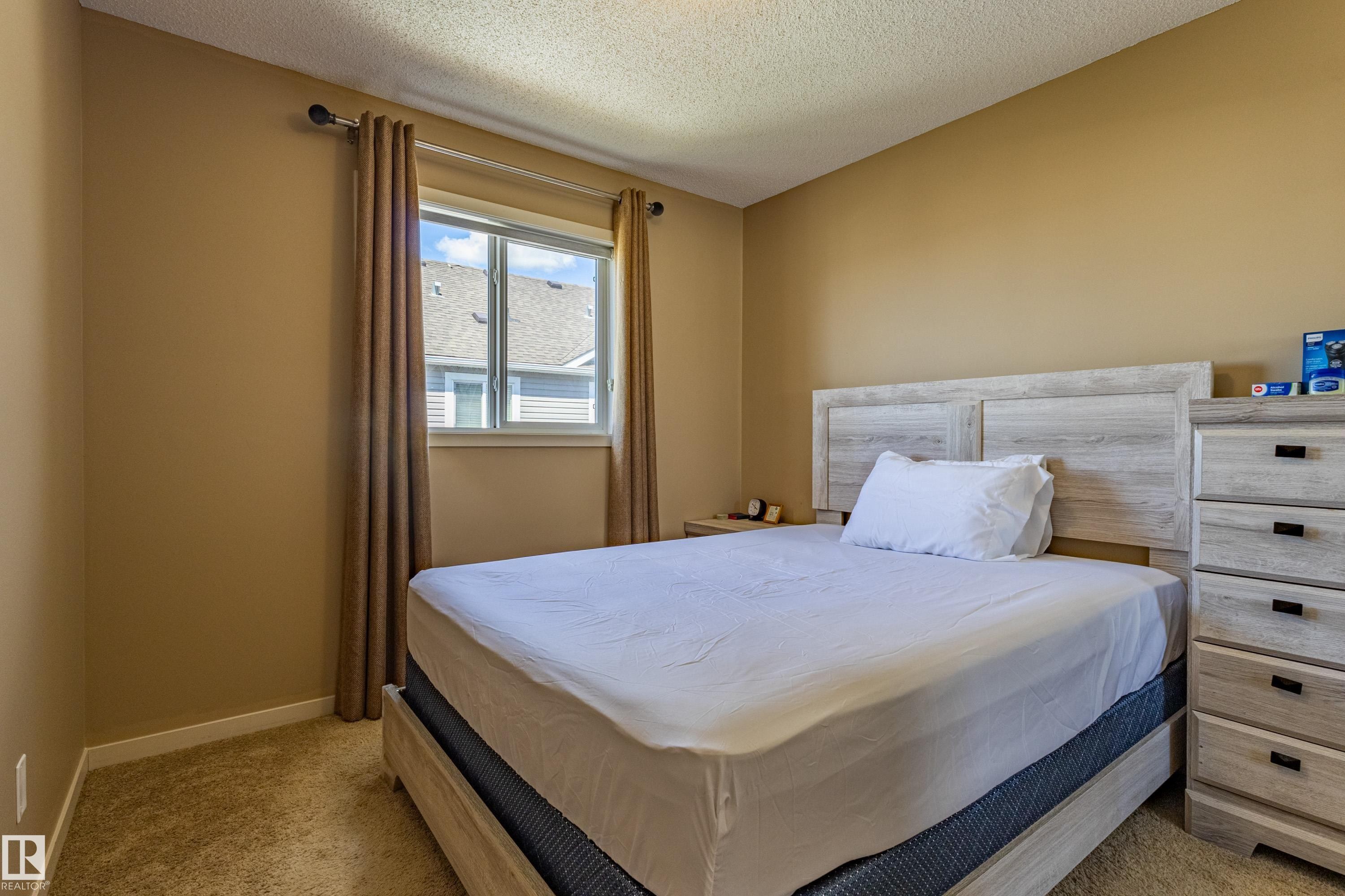 Carpeted room featuring a double-paned window with curtain rod and drapes, neutral wall color, and white trim - 13 1816 Rutherford Road, Edmonton, AB