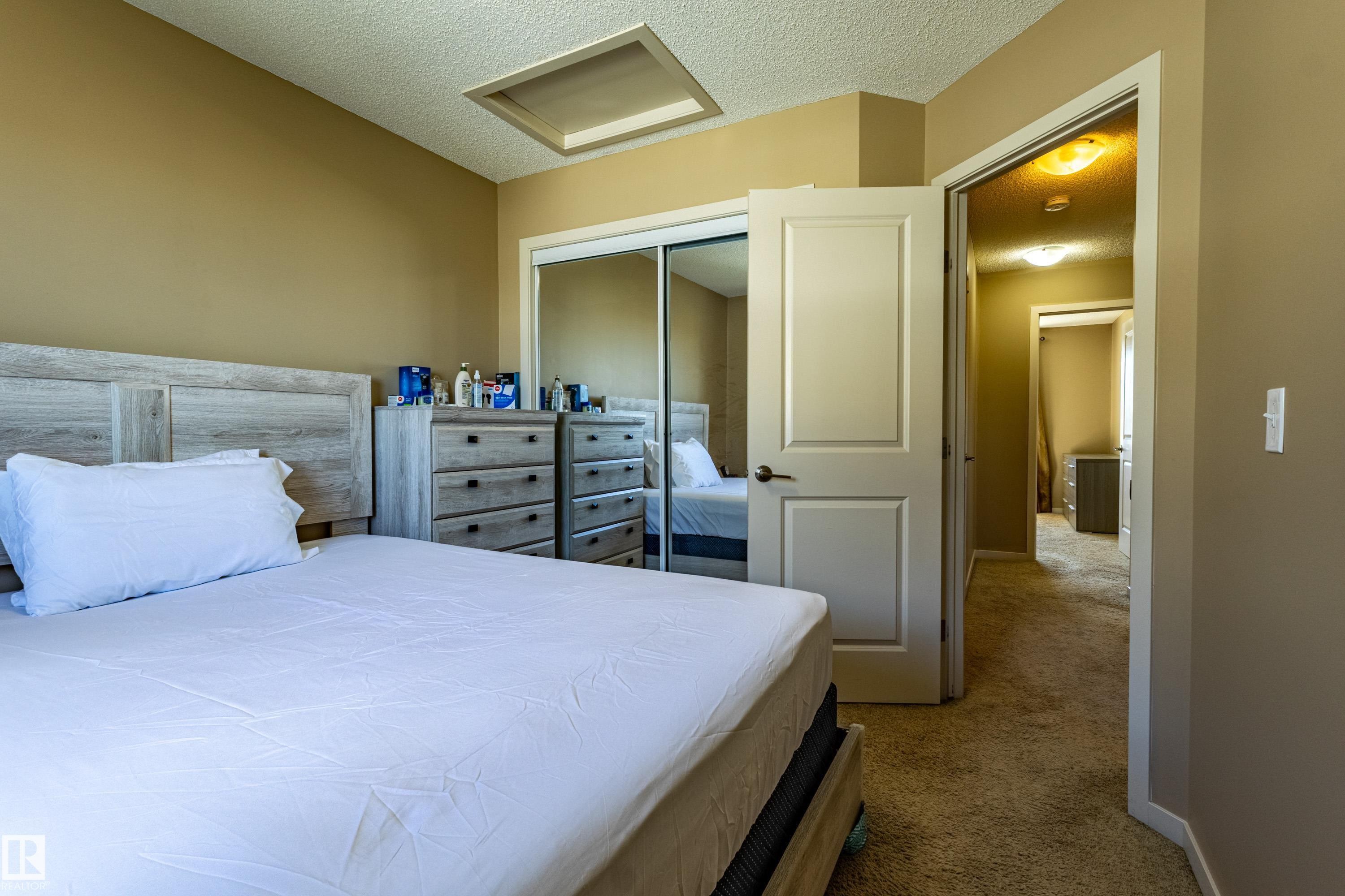 Carpeted bedroom with neutral-toned walls, a white-paneled door, and a mirrored closet - 13 1816 Rutherford Road, Edmonton, AB