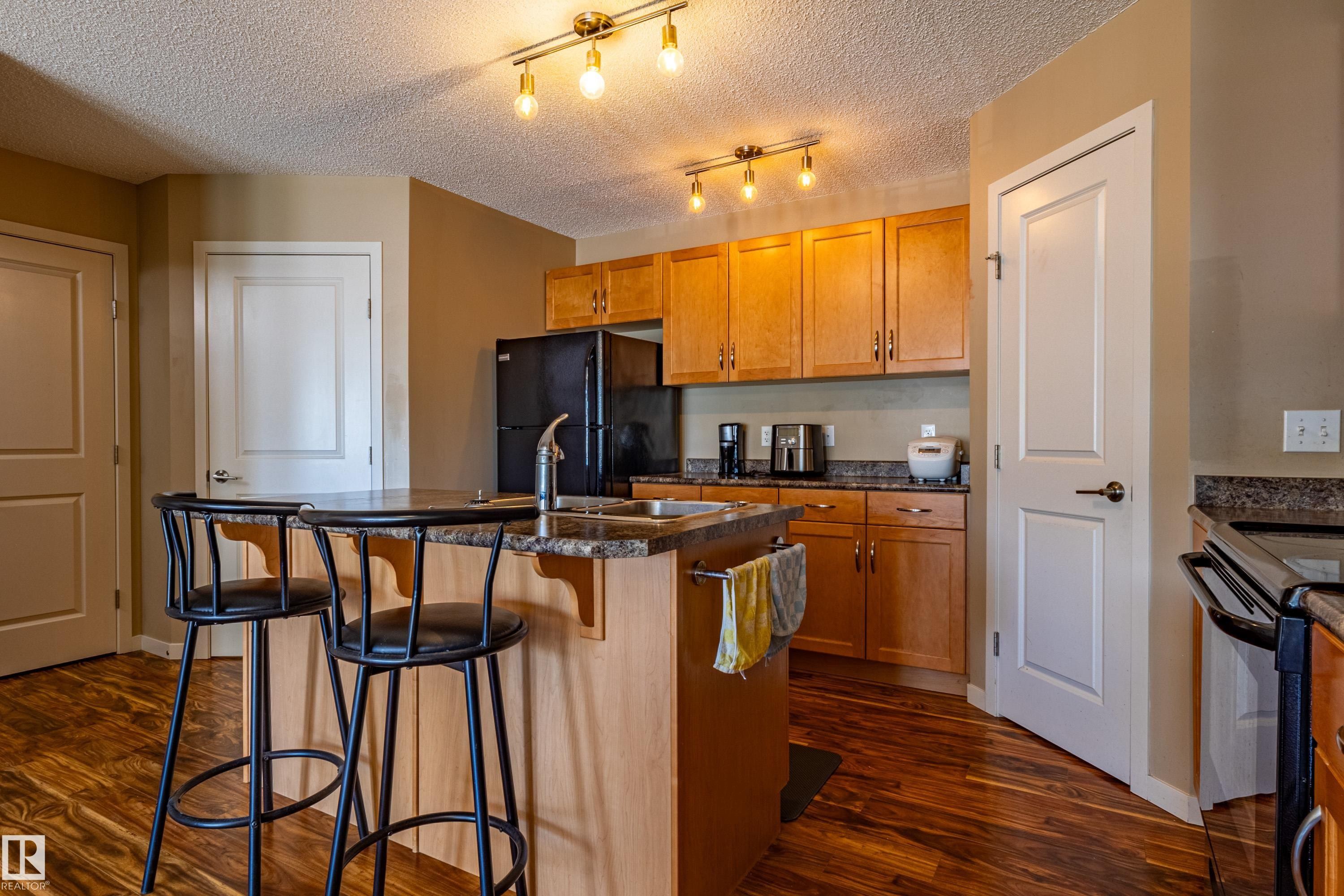 Kitchen featuring wood-finish flooring, light wood cabinetry, and track lighting - 13 1816 Rutherford Road, Edmonton, AB